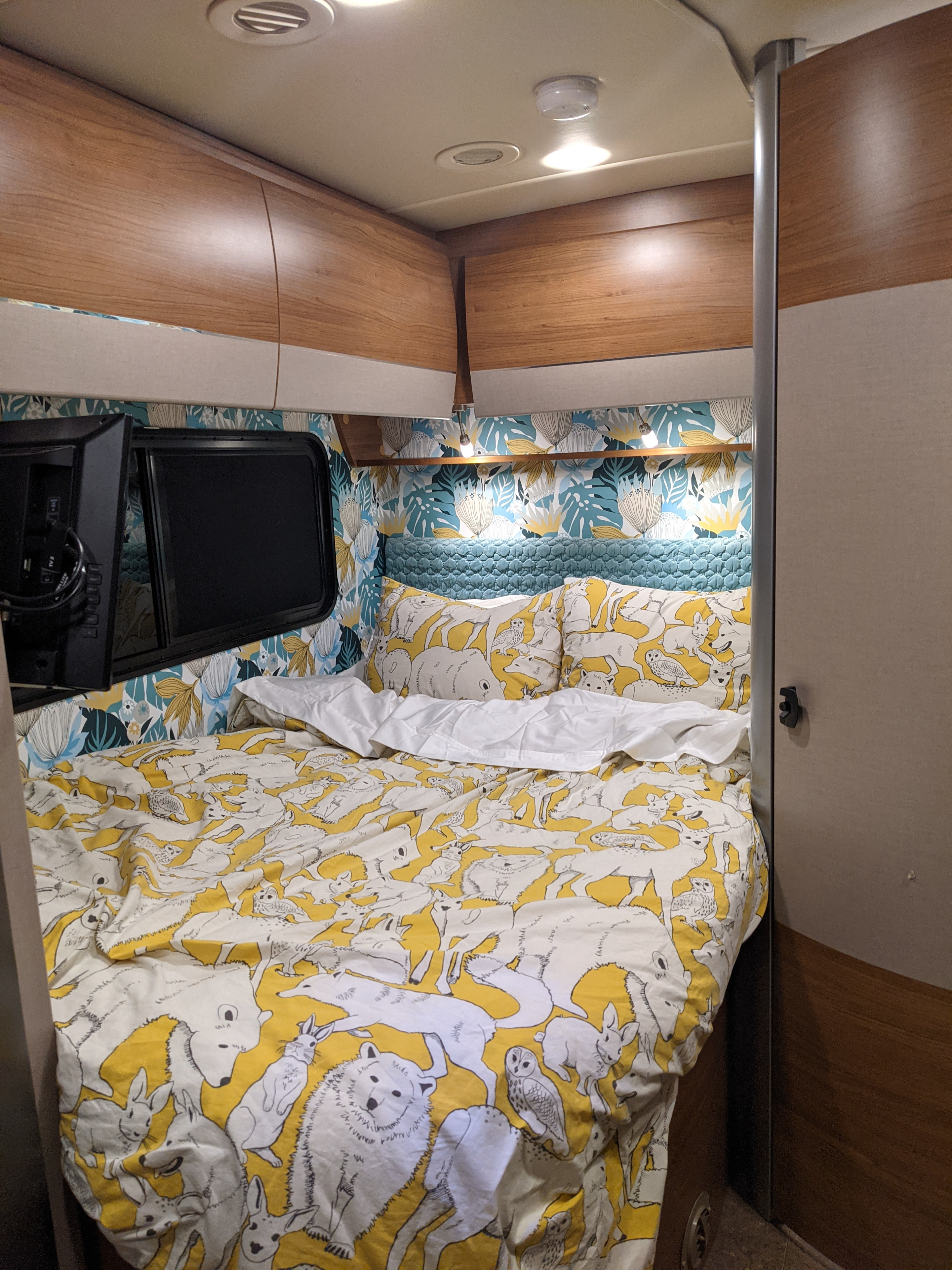 Cozy RV rental bedroom with playful animal print bedding, floral wallpaper, wood cabinets, and a mounted TV.. Winnebago Navion 2017