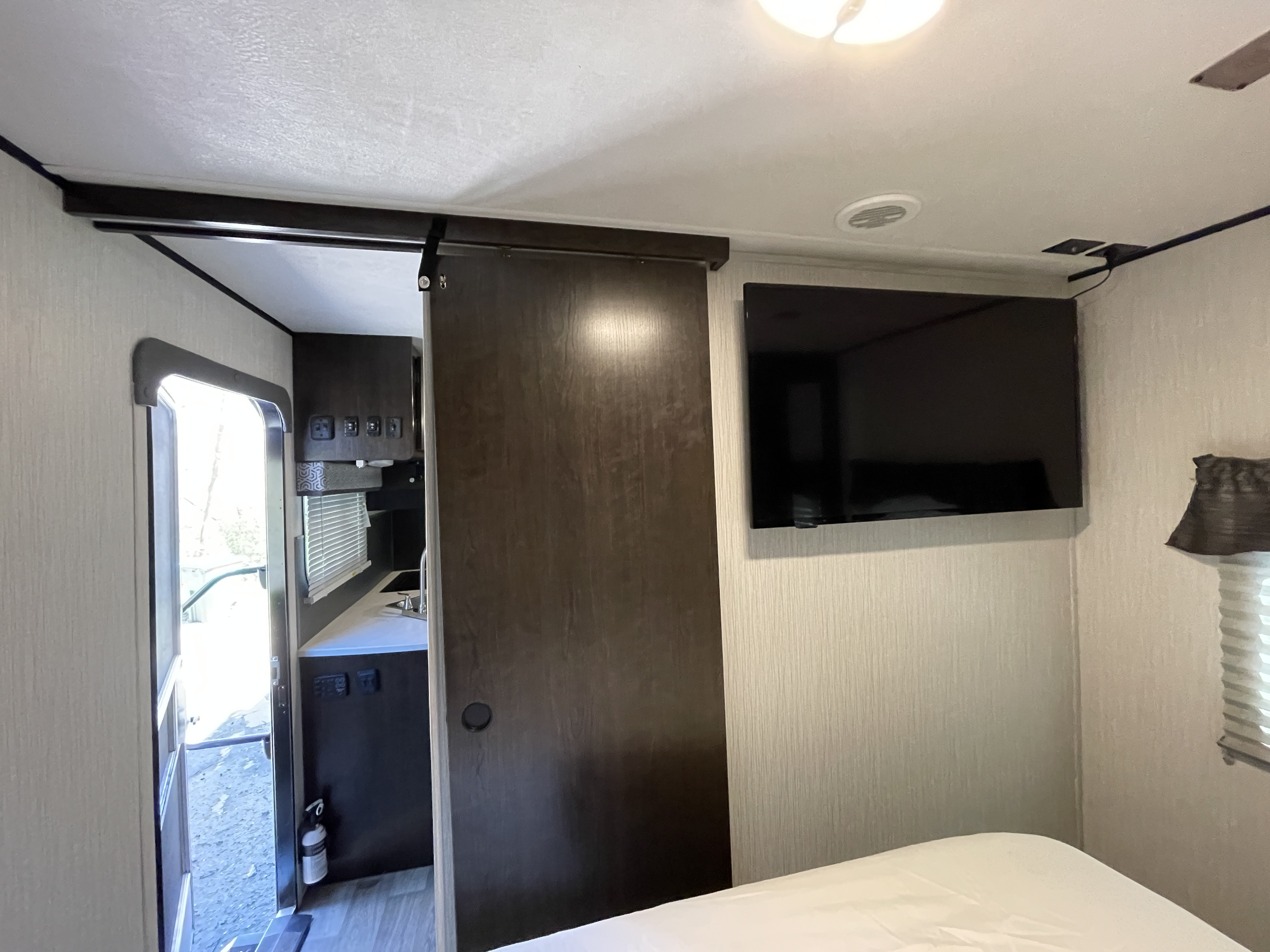 Inside a modern RV rental: a compact bedroom with a bed, a sliding door to the kitchen/galley, and a wall-mounted TV.. Heartland RVs Pioneer 2021