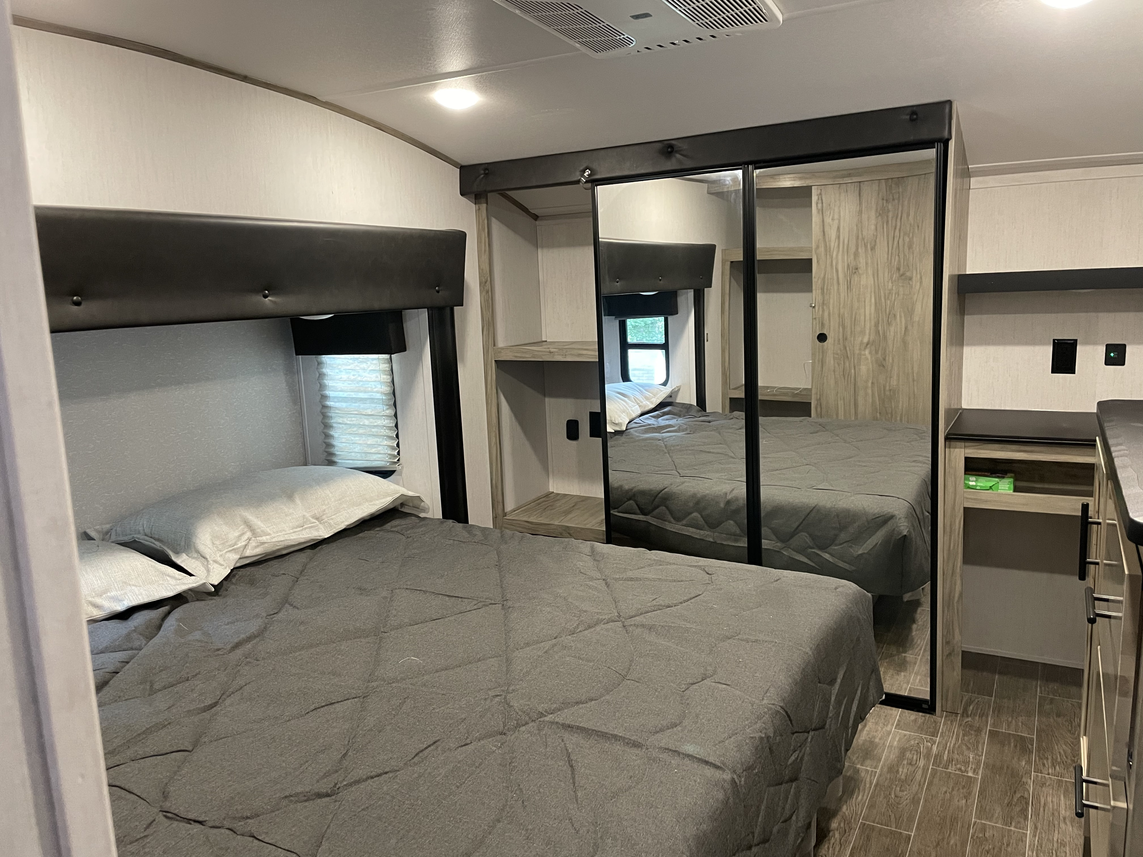 RV rental bedroom featuring a grey bed, large mirrored closet, and built-in shelving. Shows compact and functional design.. Forest River Cherokee Arctic Wolf 2022