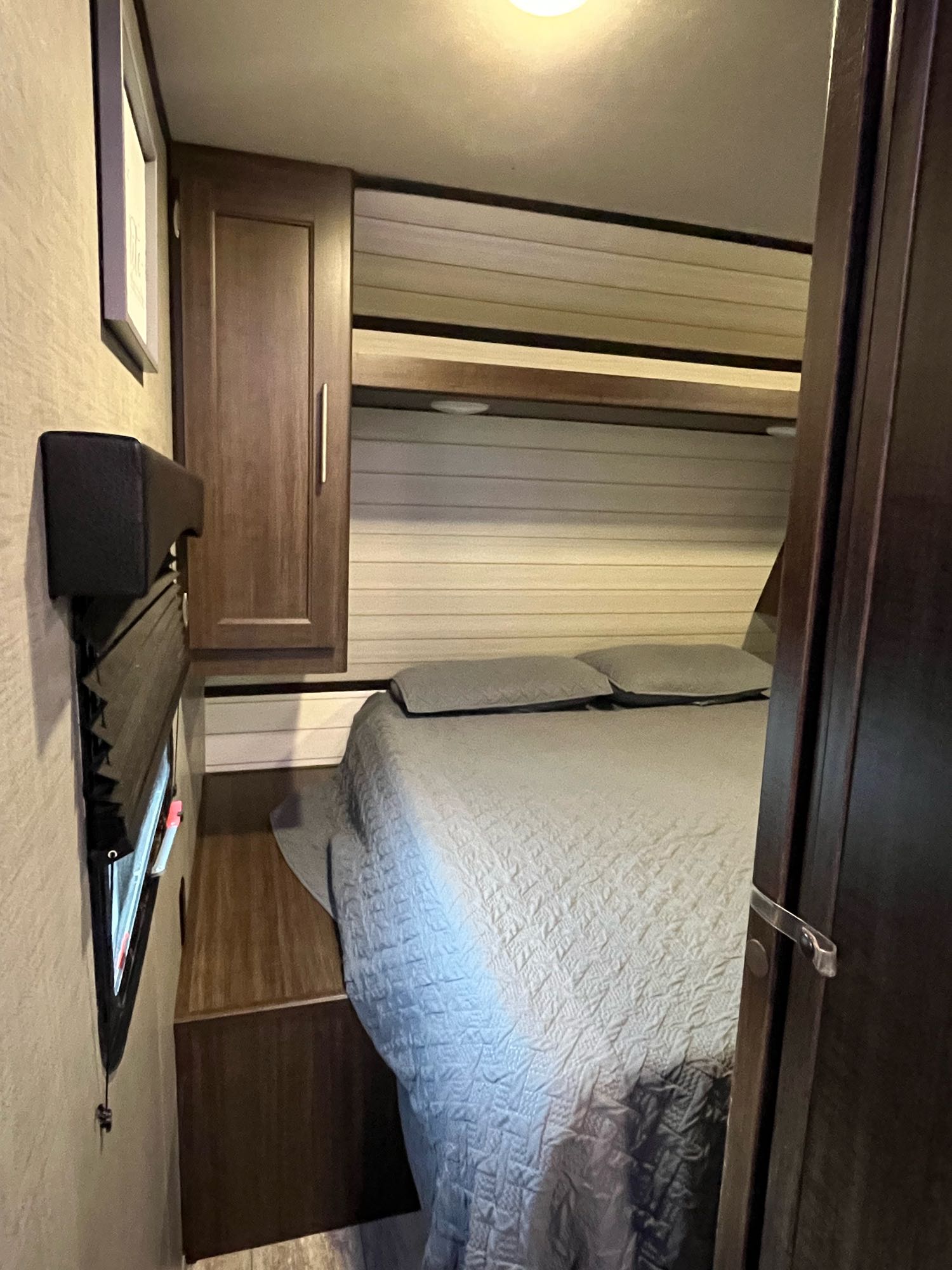 This RV rental features a comfortable bedroom with a grey quilted bed, pillows, wood cabinet, and window blinds.. Crossroads RV Zinger 2020