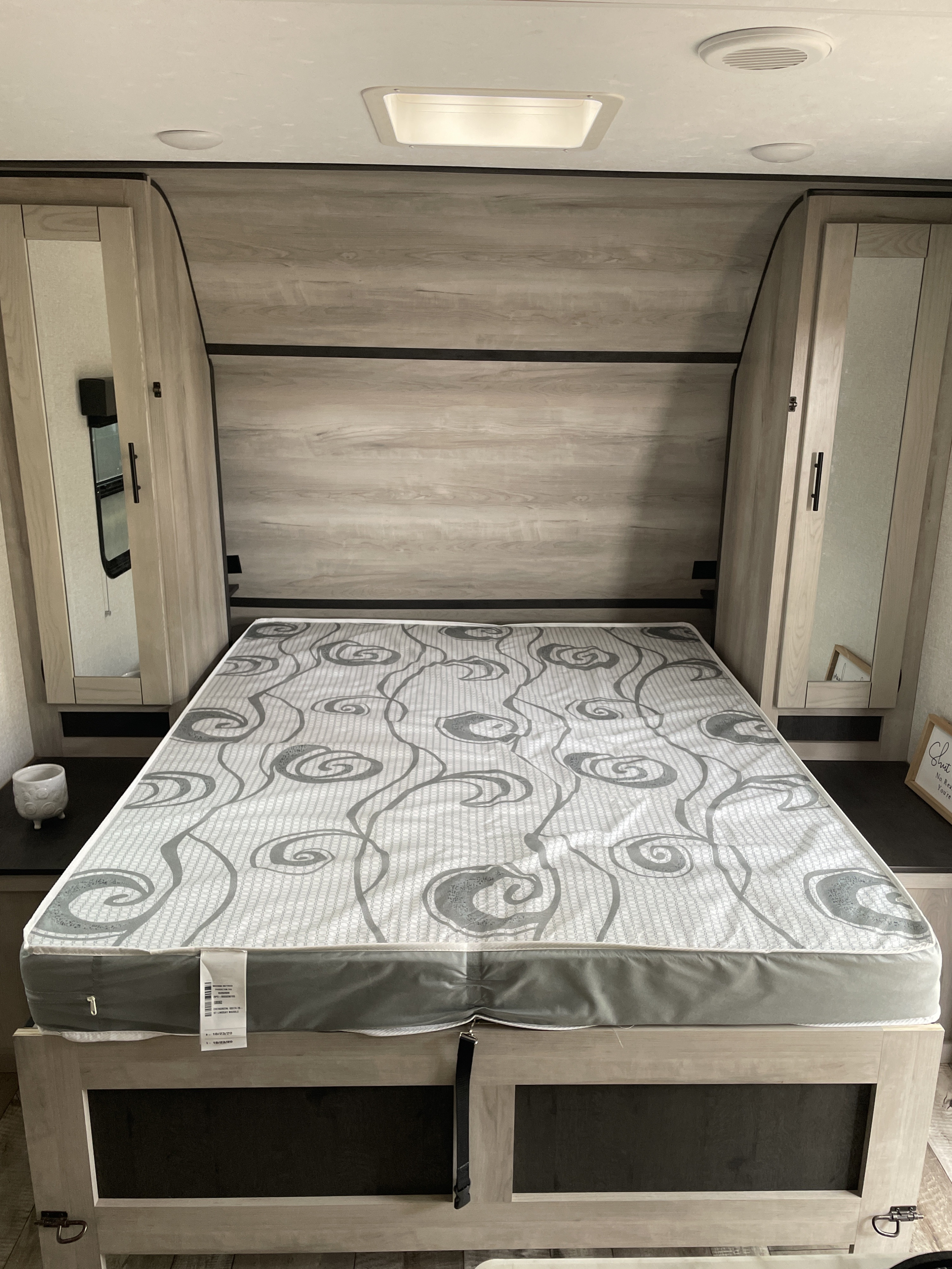 An RV rental bedroom with a grey and white patterned mattress, flanked by light wood cabinets with mirrors, and overhead lighting.. Connect SE 2021