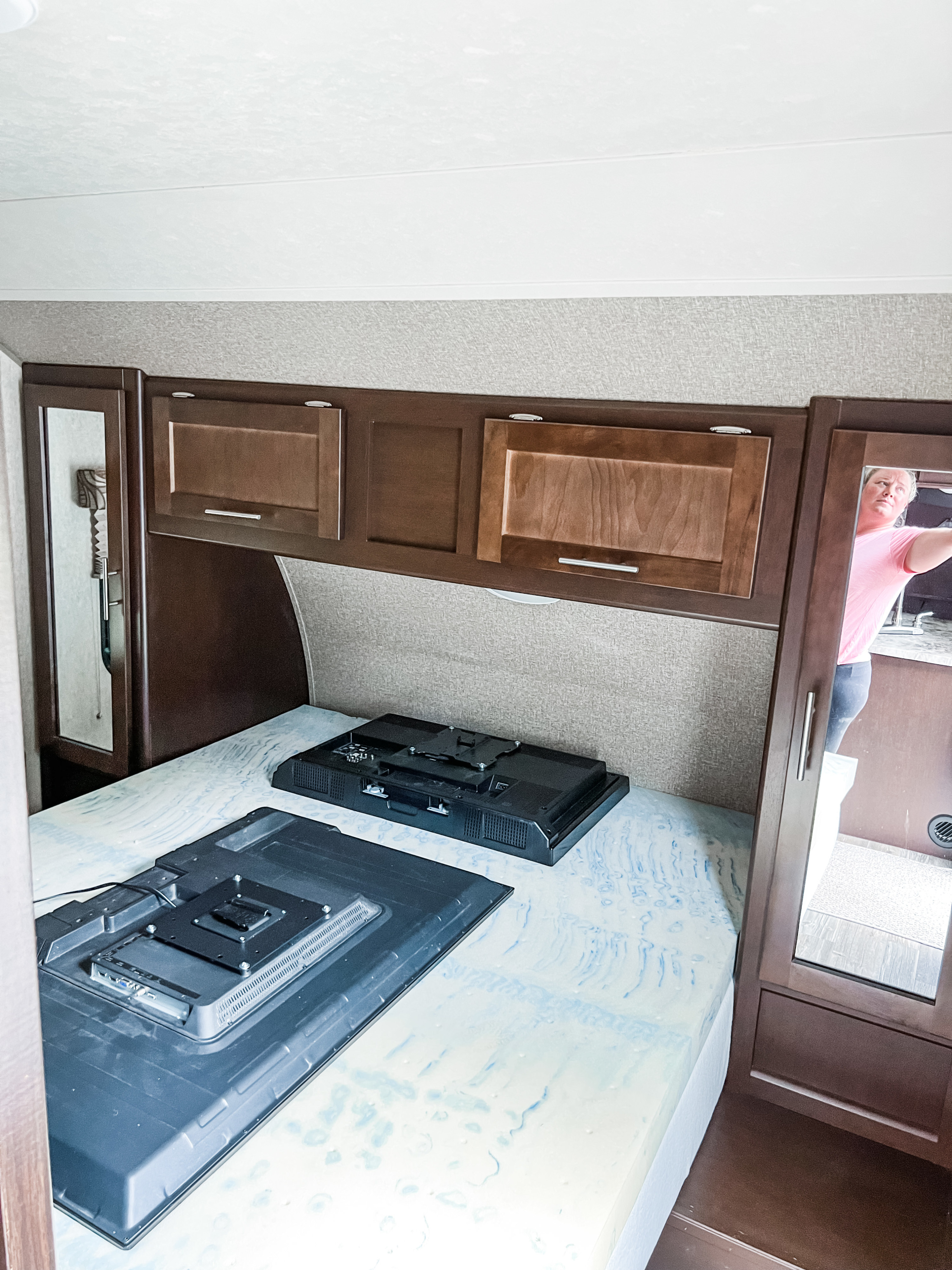 RV rental bedroom interior: two TVs on the bed, overhead cabinets, and a mirrored closet reflecting a person.. Forest River Cherokee Grey Wolf 2015