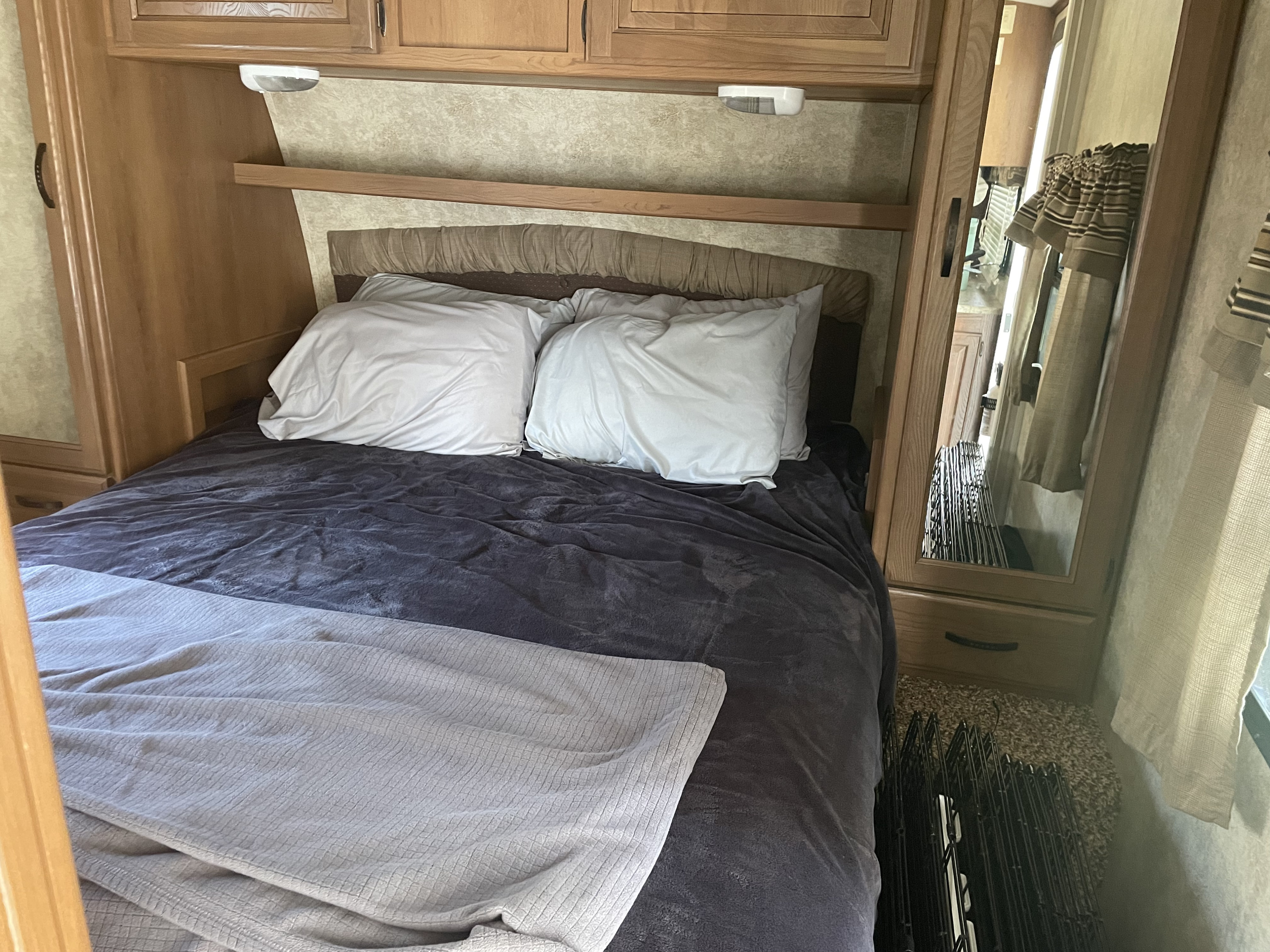 This **RV rental** bedroom features a comfy bed with dark bedding, overhead cabinets, and a mirrored wardrobe.. Keystone RV Outback 2013