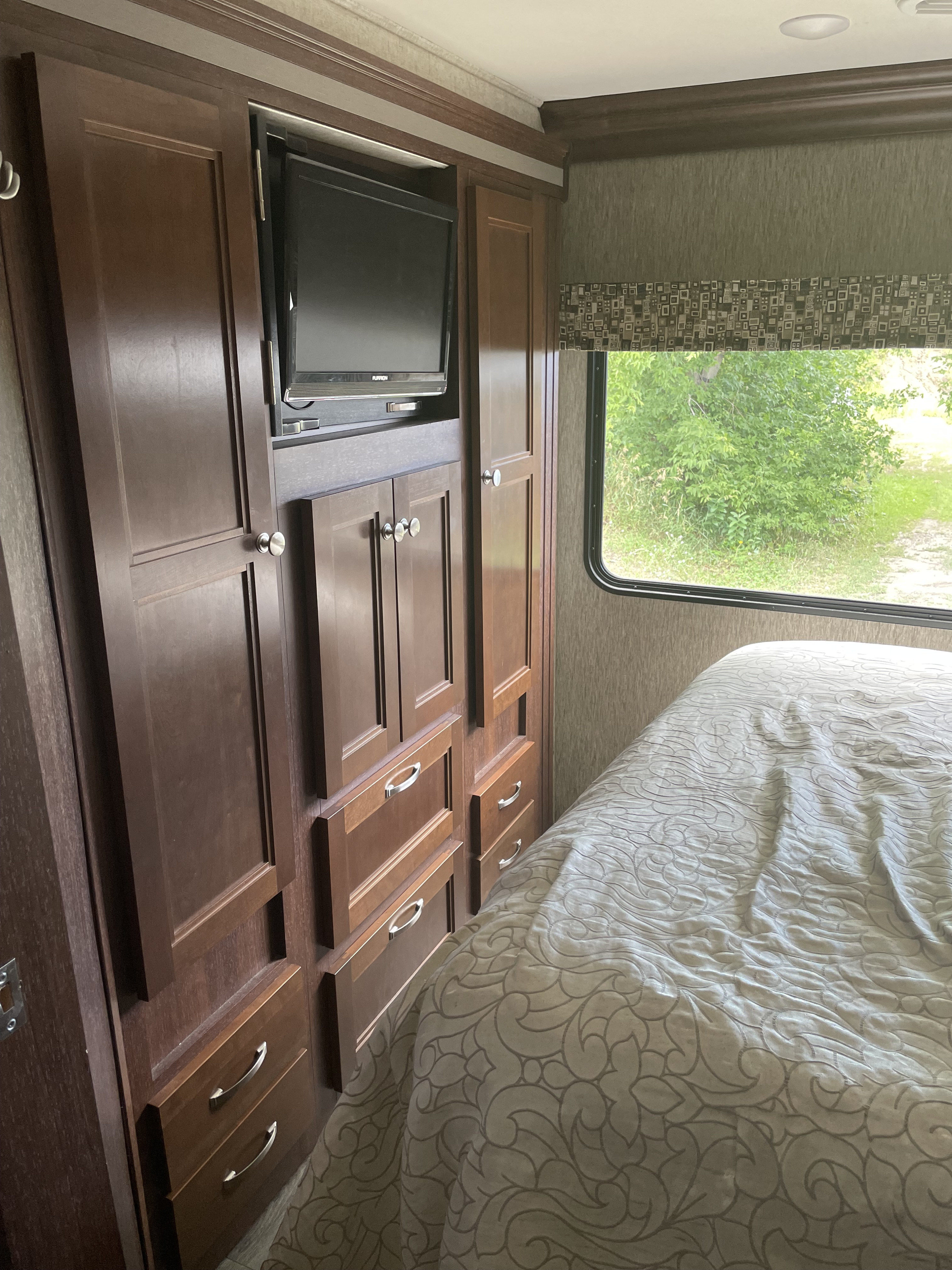This RV rental bedroom features a dark wood cabinet with a built-in TV, drawers, and a cozy bed by a window.. Forest River Sunseeker 2017