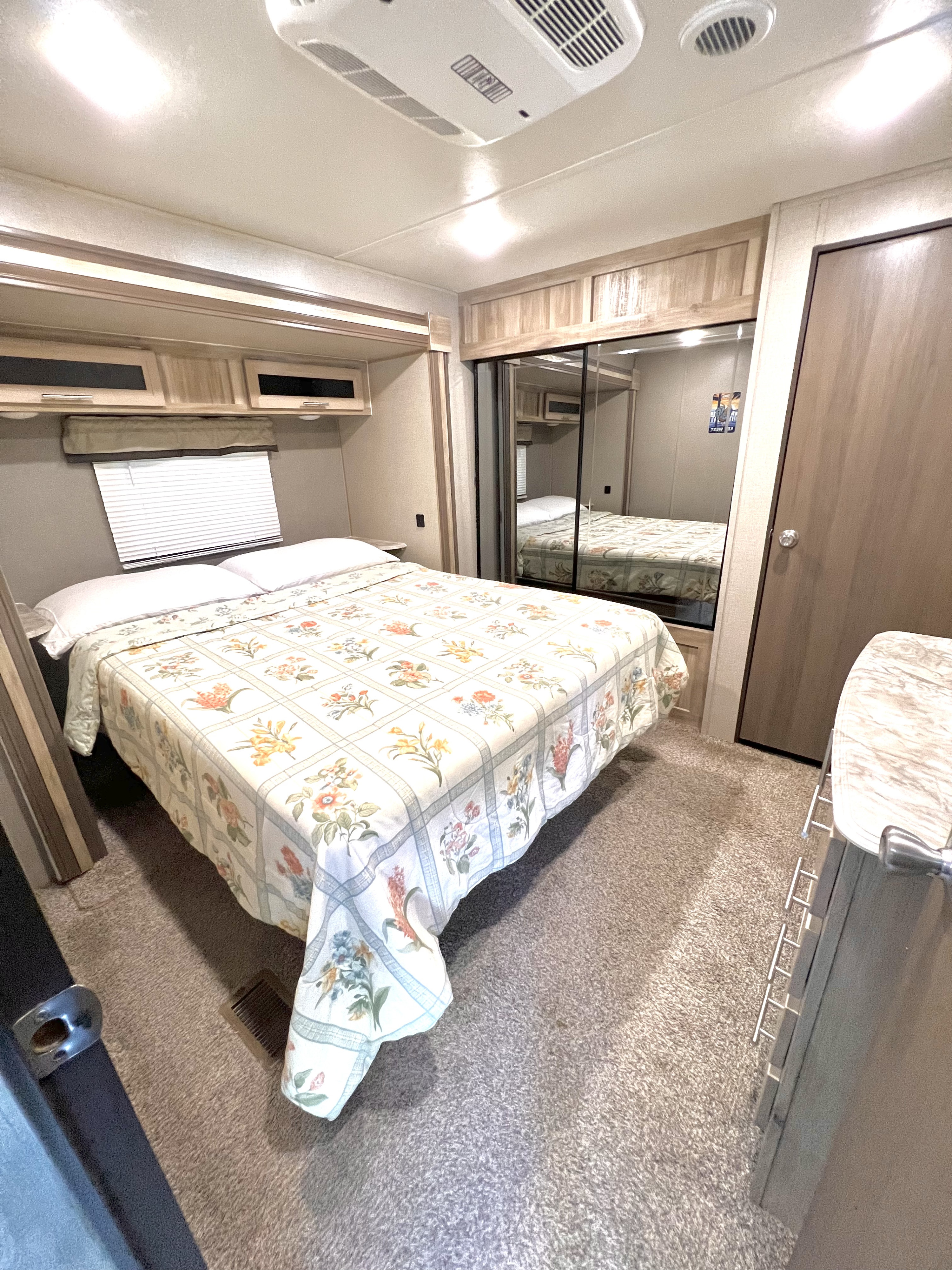 Step into this cozy RV rental bedroom featuring a floral bed, mirrored closet, and practical overhead storage.. Catalina Legacy 343BHTS 2021