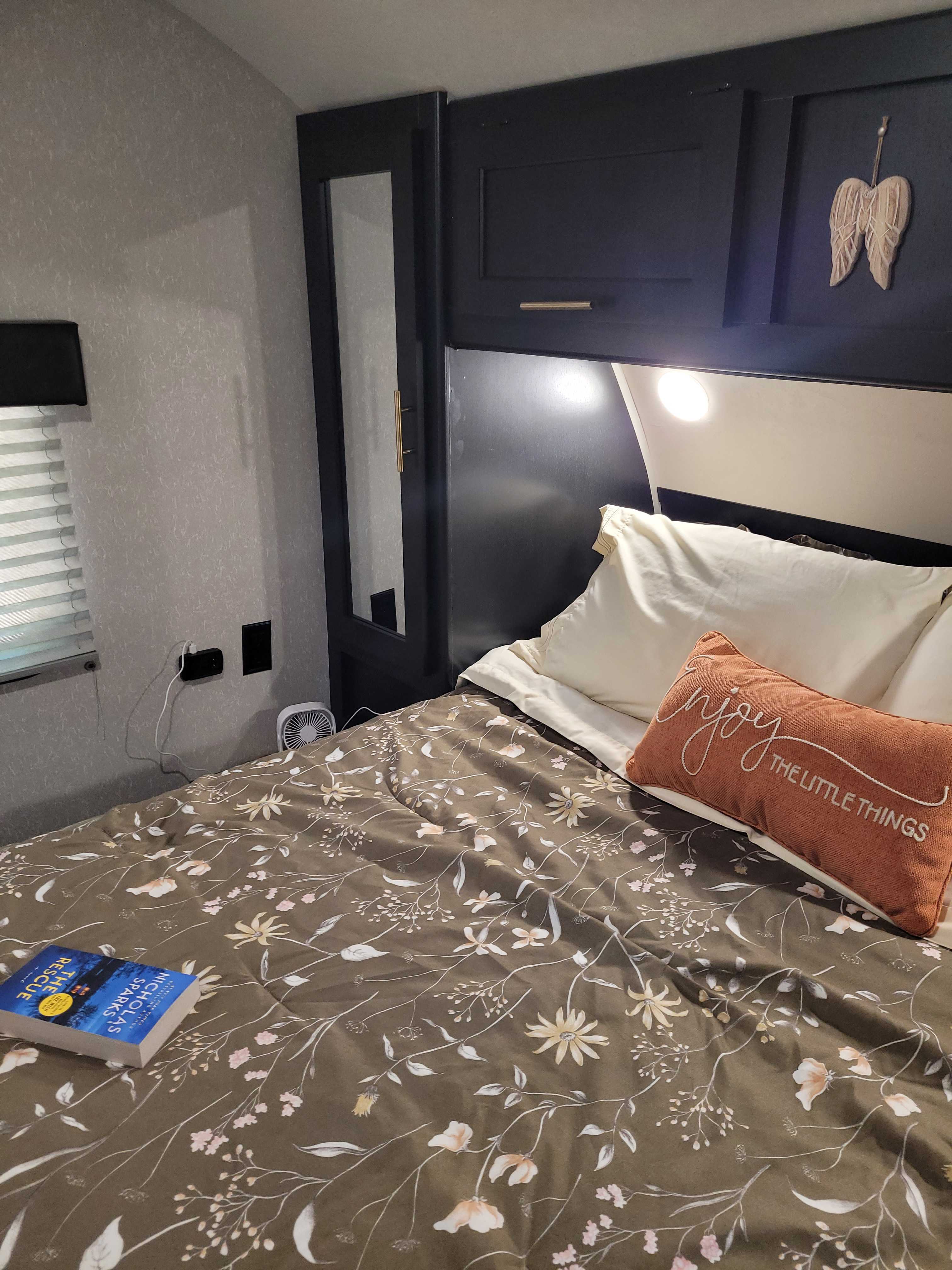 Enjoy a cozy night in this well-appointed RV rental bedroom, featuring floral bedding, built-in storage, & mood lighting.. Forest River Cherokee 2021