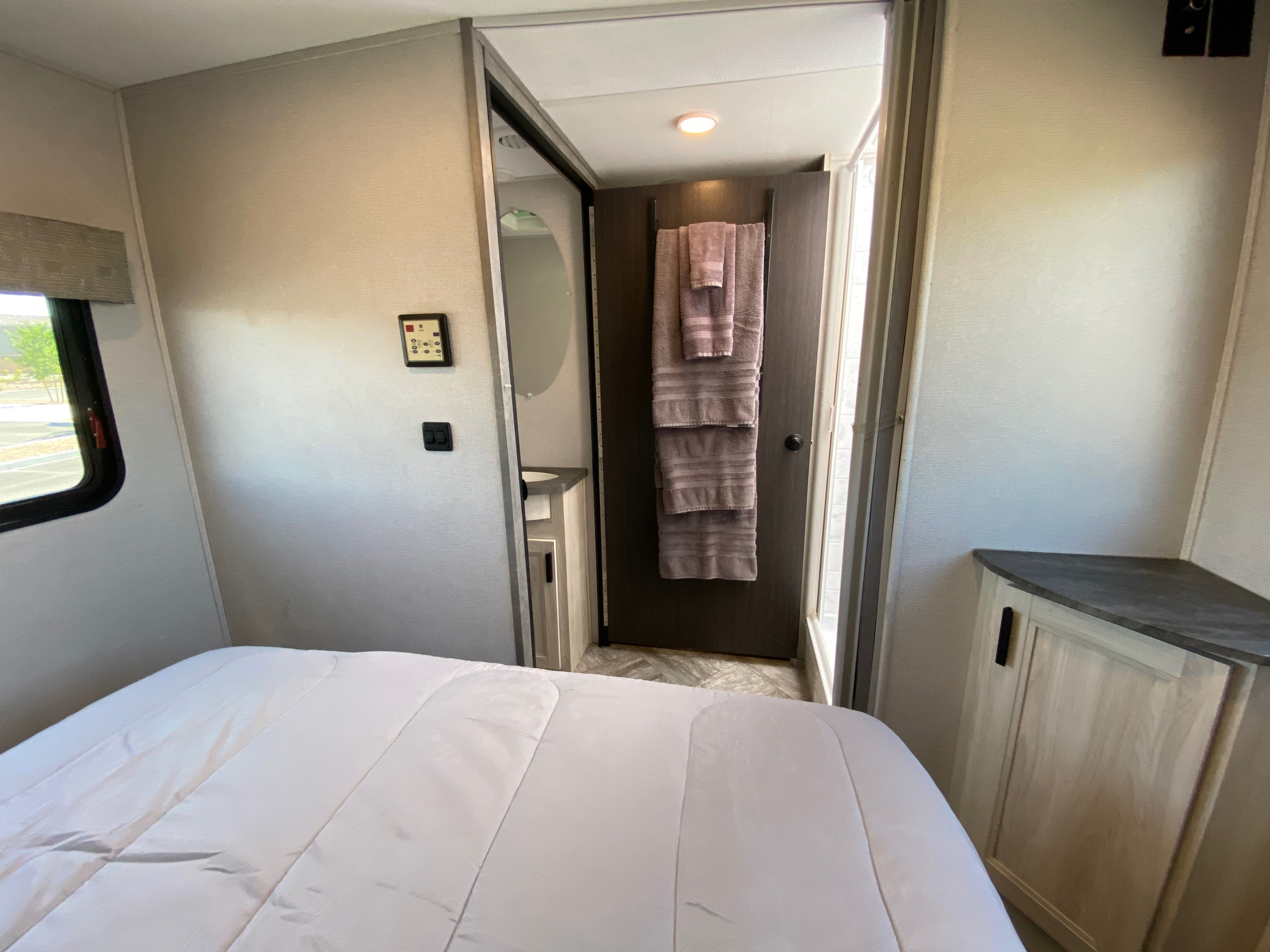 RV rental interior featuring a cozy bedroom with a white bed, leading to a functional bathroom with towels.. Forest River Sunseeker LE 2022