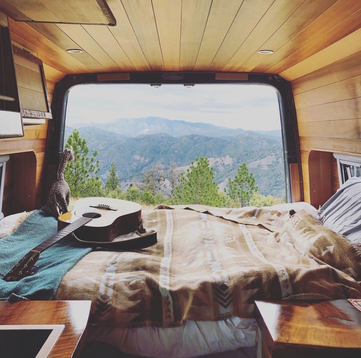 Experience van life: Cozy RV rental bedroom with guitar & giraffe, offering panoramic mountain views from open rear doors.. Mercedes-Benz Sprinter 2019