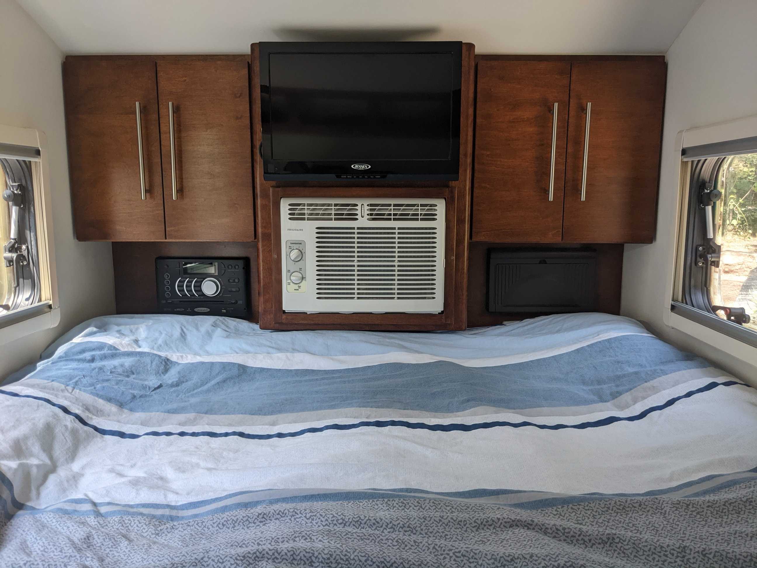 Cozy RV rental bedroom with striped bedding, built-in cabinets, TV, and AC unit for comfortable stays.. T@G T@G Trailer 2016
