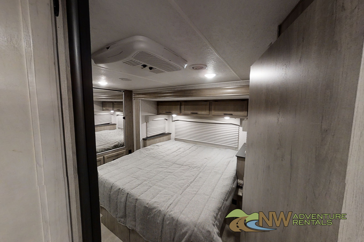 Explore the comfortable bedroom of this RV rental, complete with a queen bed, storage, and AC for a relaxing trip.. Coachmen Freelander 2021