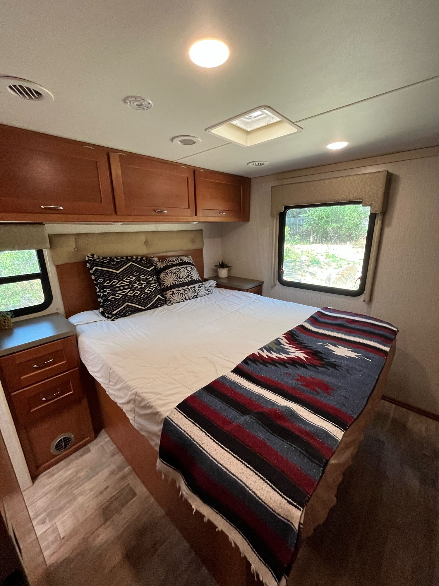 Cozy RV rental bedroom with warm wood cabinets, a comfy bed, patterned pillows, and a vibrant blanket.. Winnebago Minnie Winnie 2017
