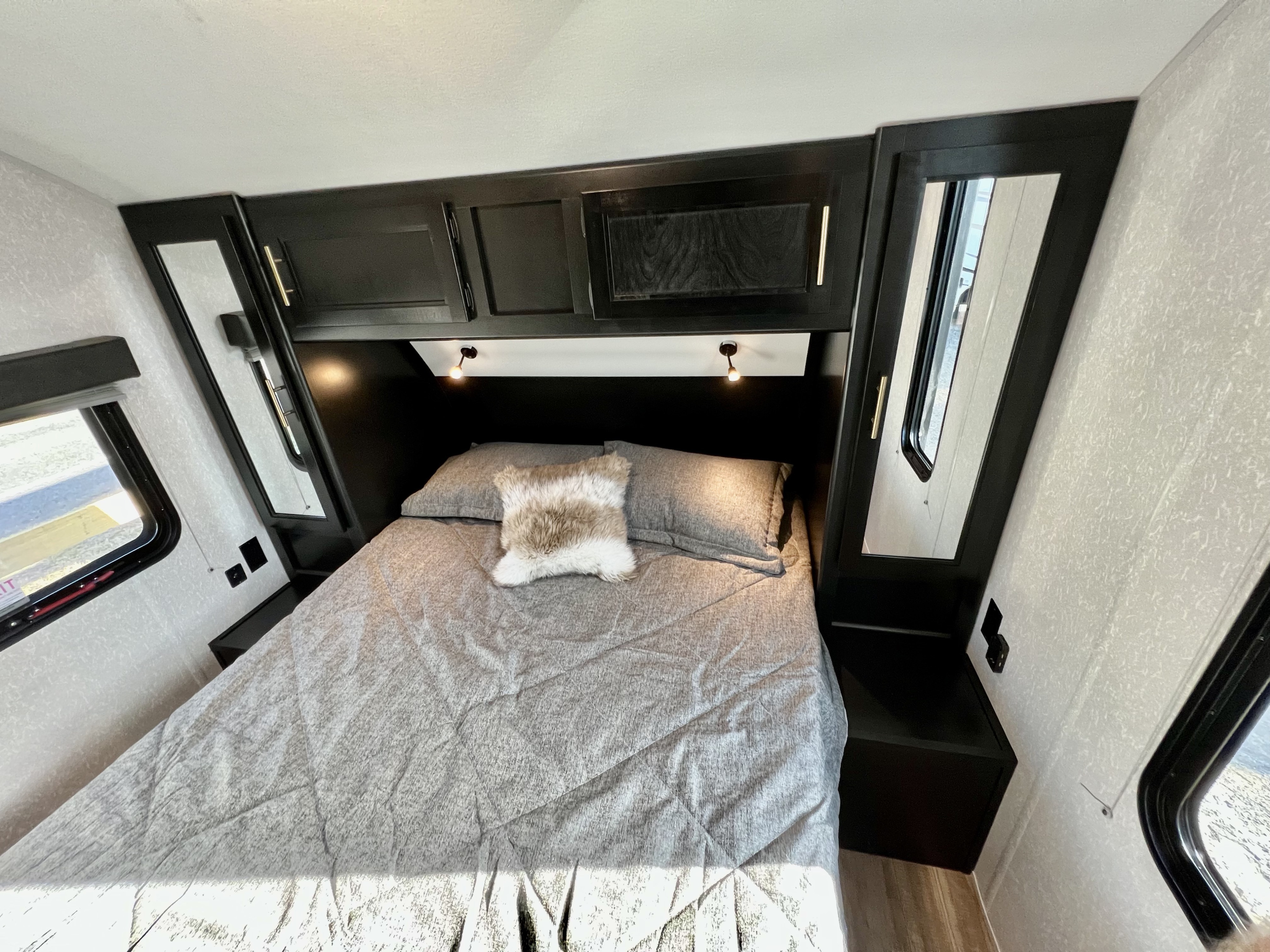 Inside a modern RV rental bedroom featuring a comfy bed, dark wood cabinets, overhead lighting, and mirrored wardrobes.. Forest River Cherokee Grey Wolf 2022