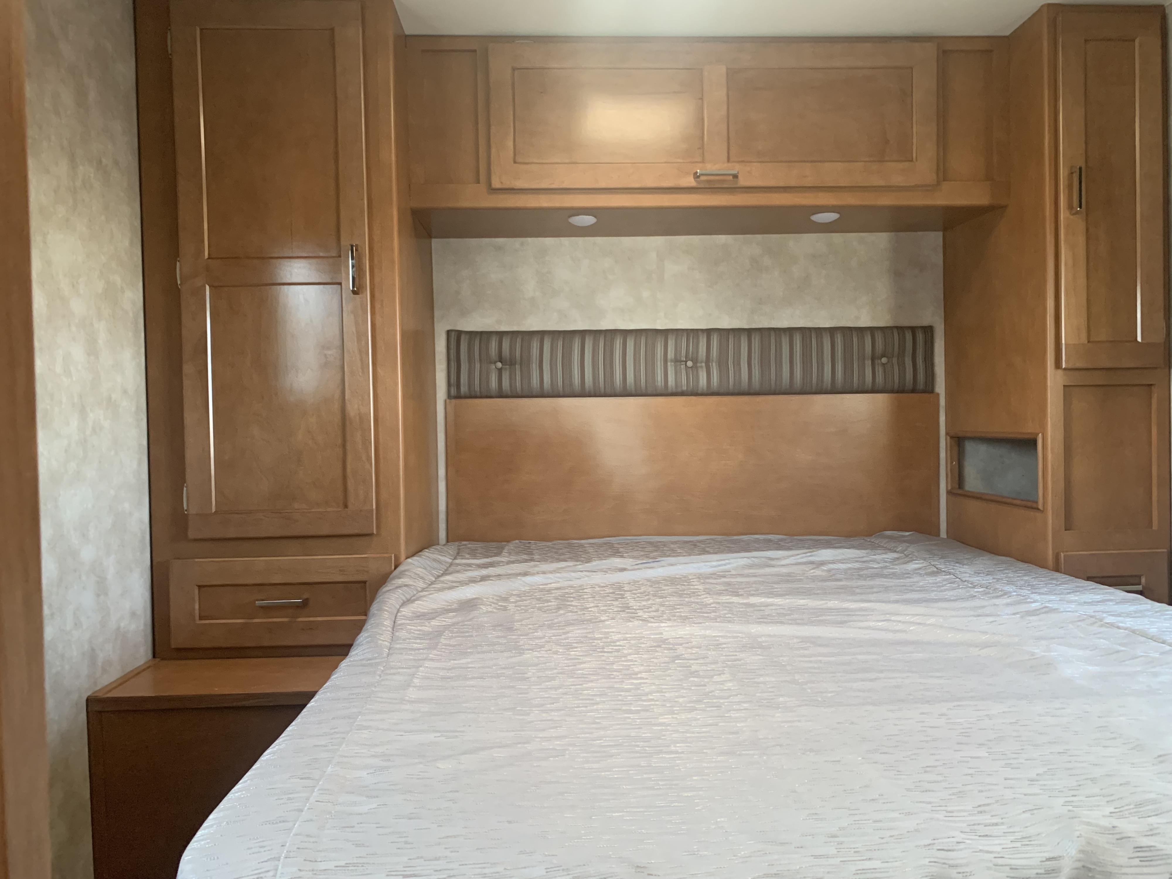 Explore this RV rental's bedroom: a comfy bed with a striped headboard, flanked by light wooden cabinets.. Winnebago Minnie Winnie 2019