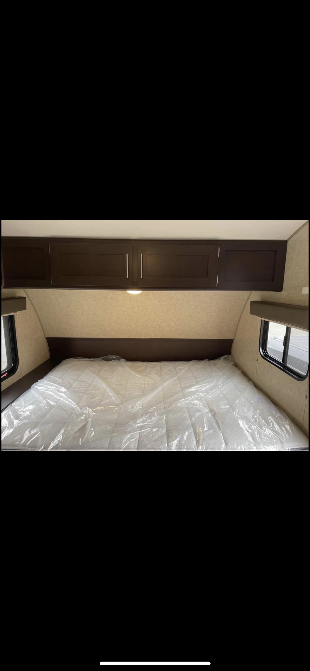 Inside an RV rental: a pristine bedroom featuring a plastic-wrapped mattress, dark overhead cabinets, and side windows.. Forest River Cherokee Wolf Pup 2018