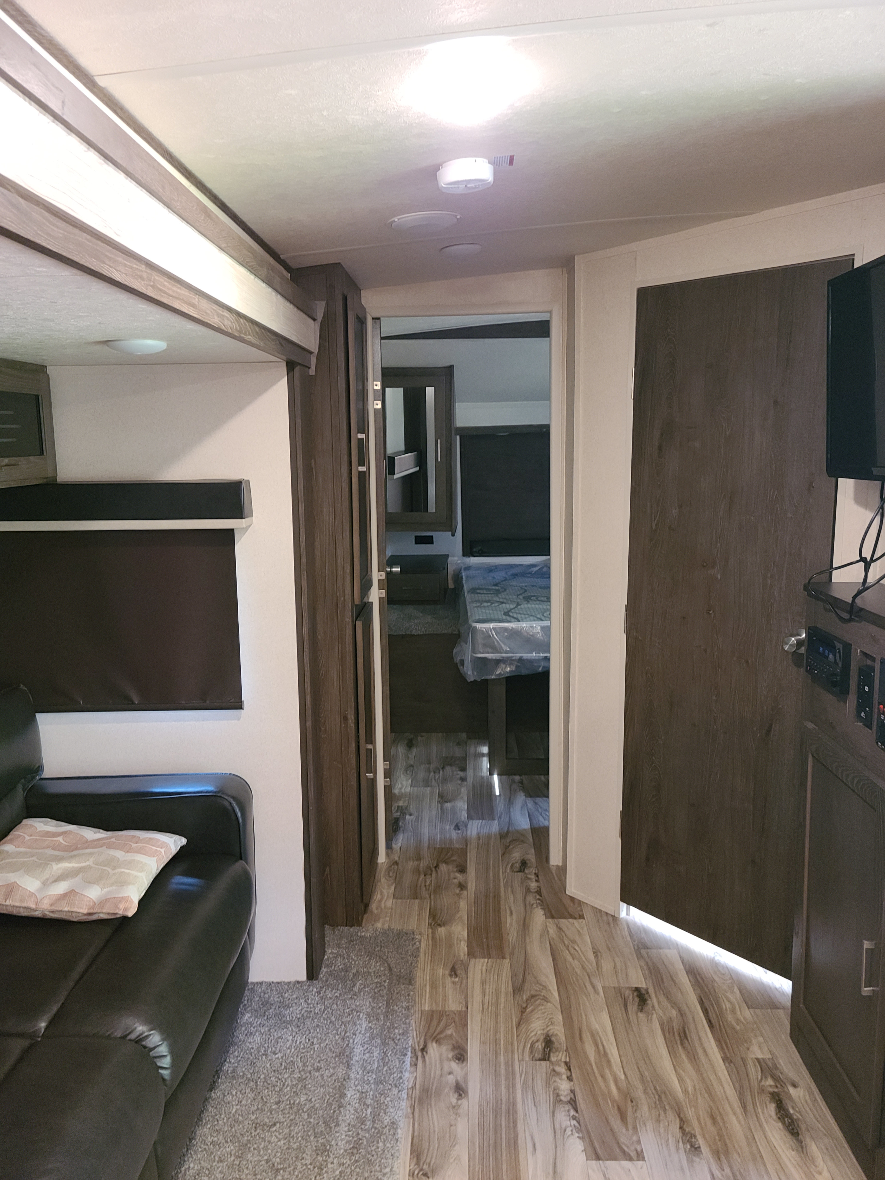 Modern RV rental interior: view from the living room with a dark sofa, leading through a wood-look hallway to the bedroom.. Forest River Salem Hemisphere GLX 2019