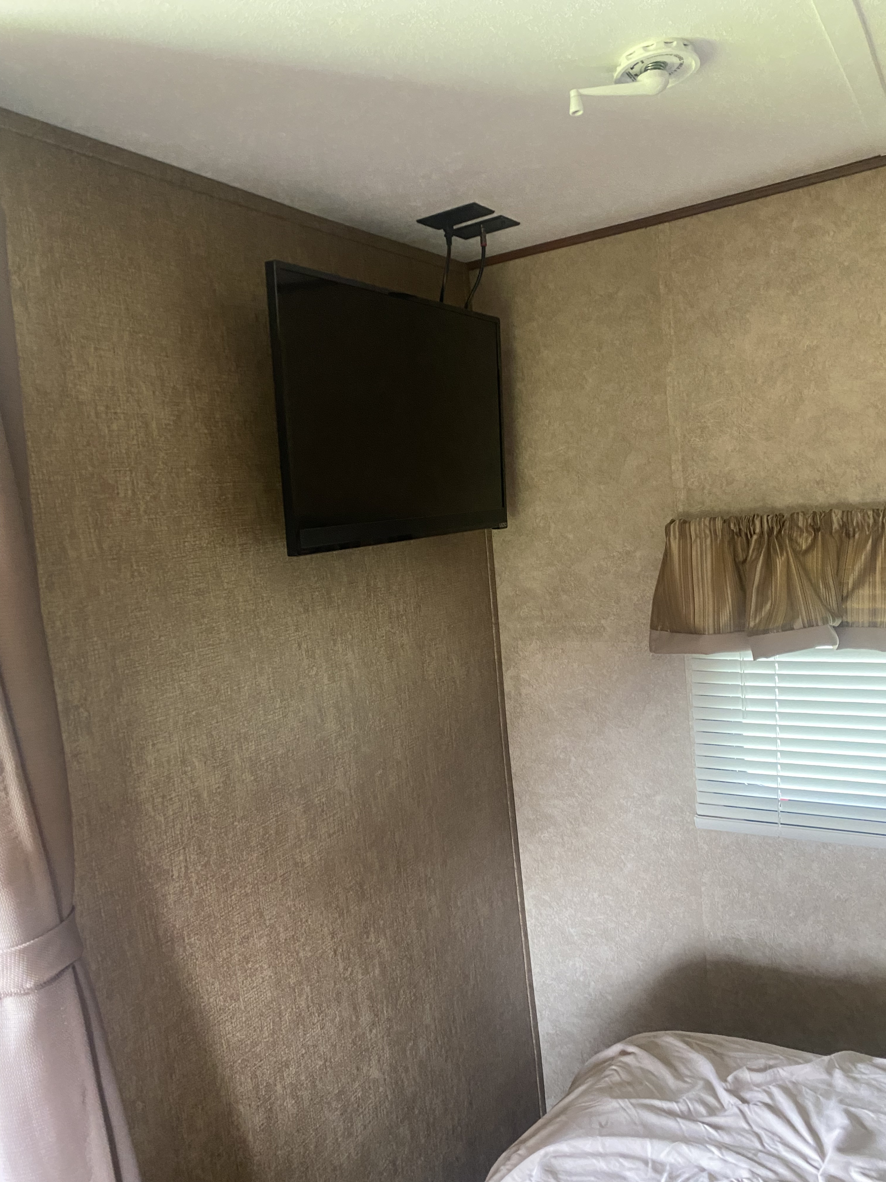 Cozy RV rental bedroom with a mounted TV, perfect for entertainment on the go. Features a bed and window with blinds.. Avenger ATI 2015