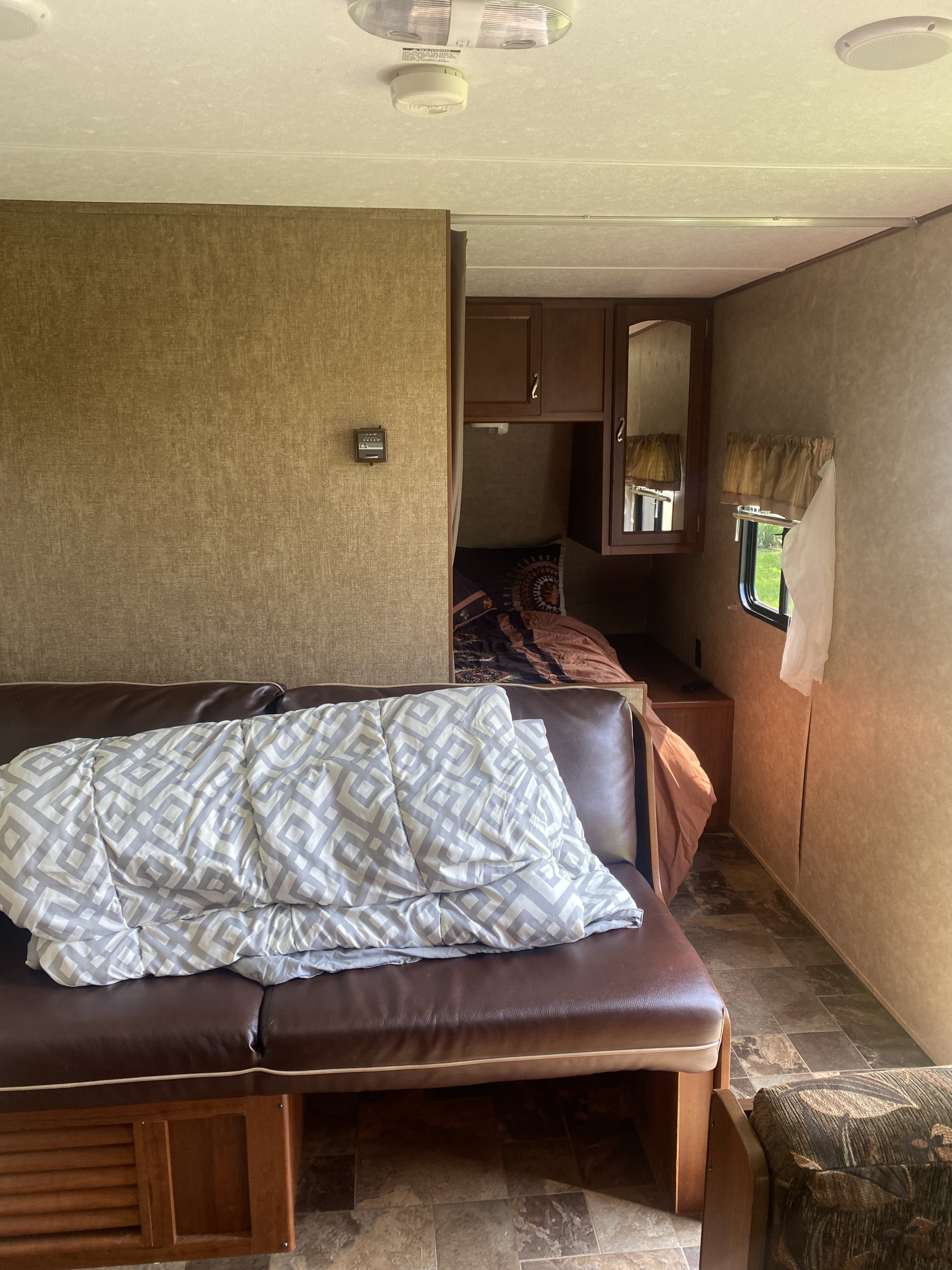 Inside a cozy rv rental: living area with sofa and patterned blanket, plus a compact bedroom, perfect for journeys.. Avenger ATI 2015