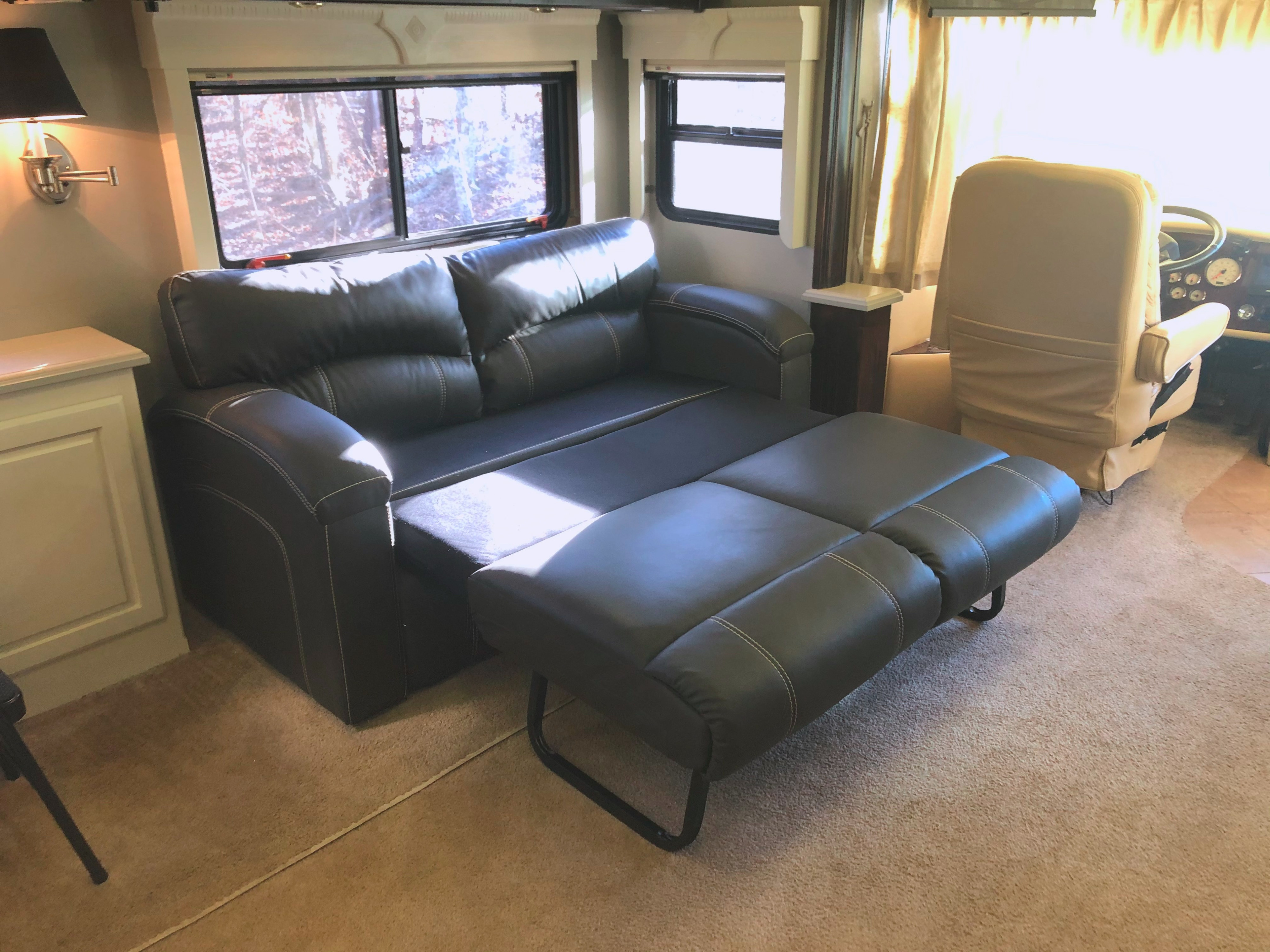 Interior of an RV rental showing a dark leather sofa pulled out into a bed, with windows and carpet.. Monaco Windsor 2004