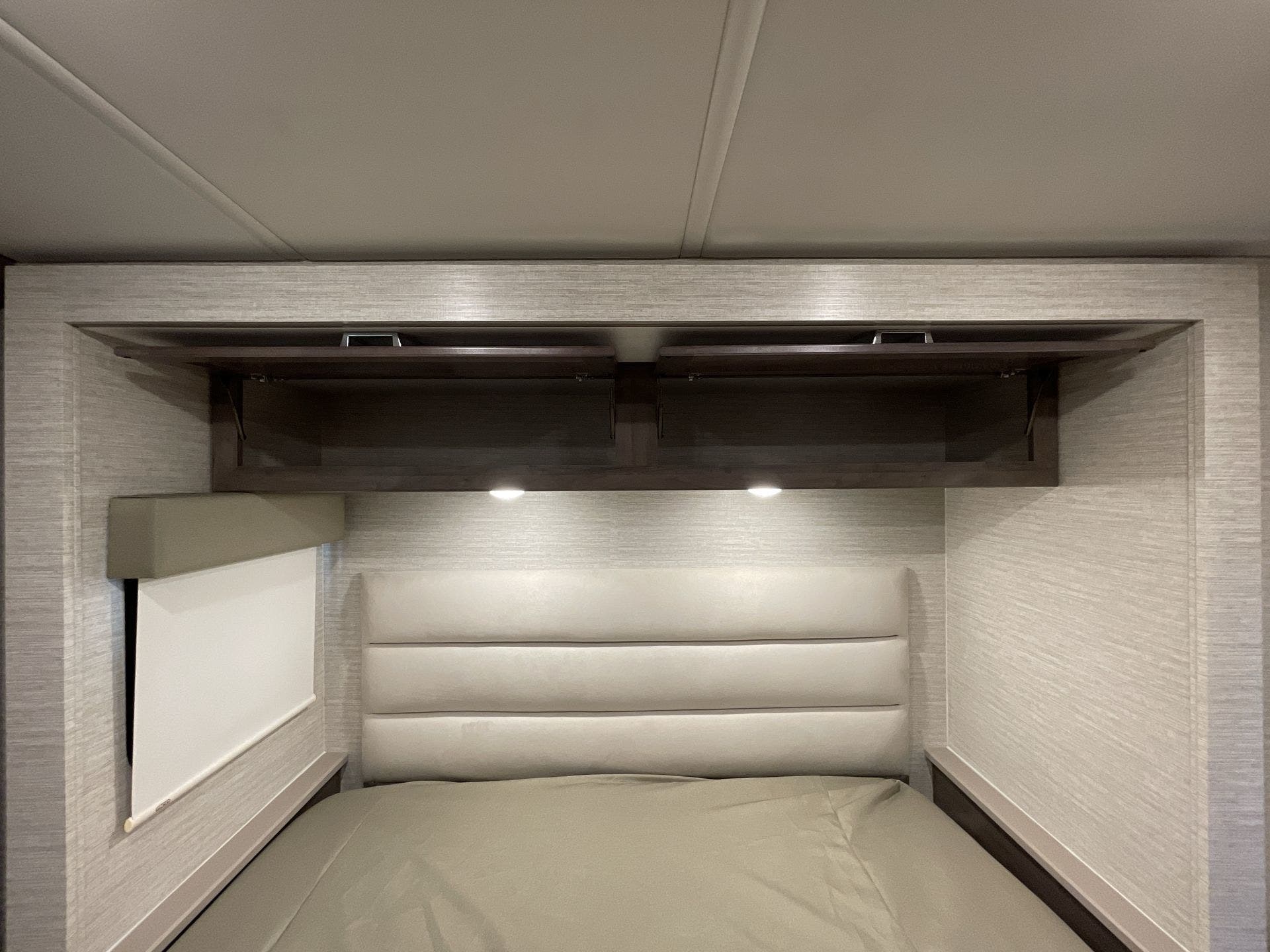 Inside an RV rental: a modern bedroom with a comfy bed, padded headboard, open overhead cabinets, and reading lights.. Winnebago Sunstar 2022