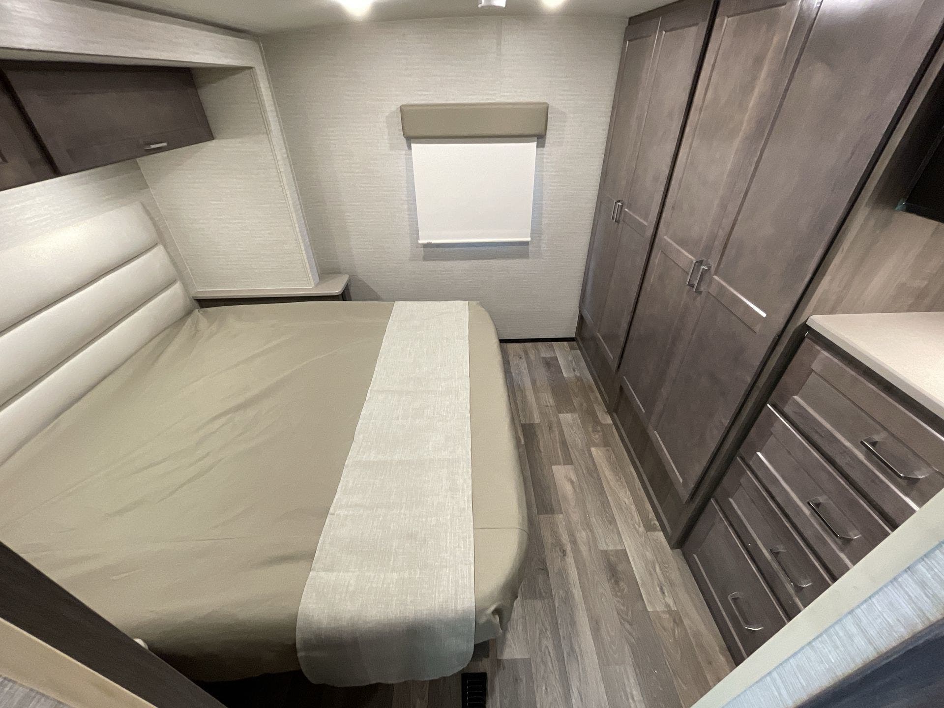 RV rental's cozy bedroom features a bed, modern wood-toned storage cabinets, and a window for comfortable travel.. Winnebago Sunstar 2022