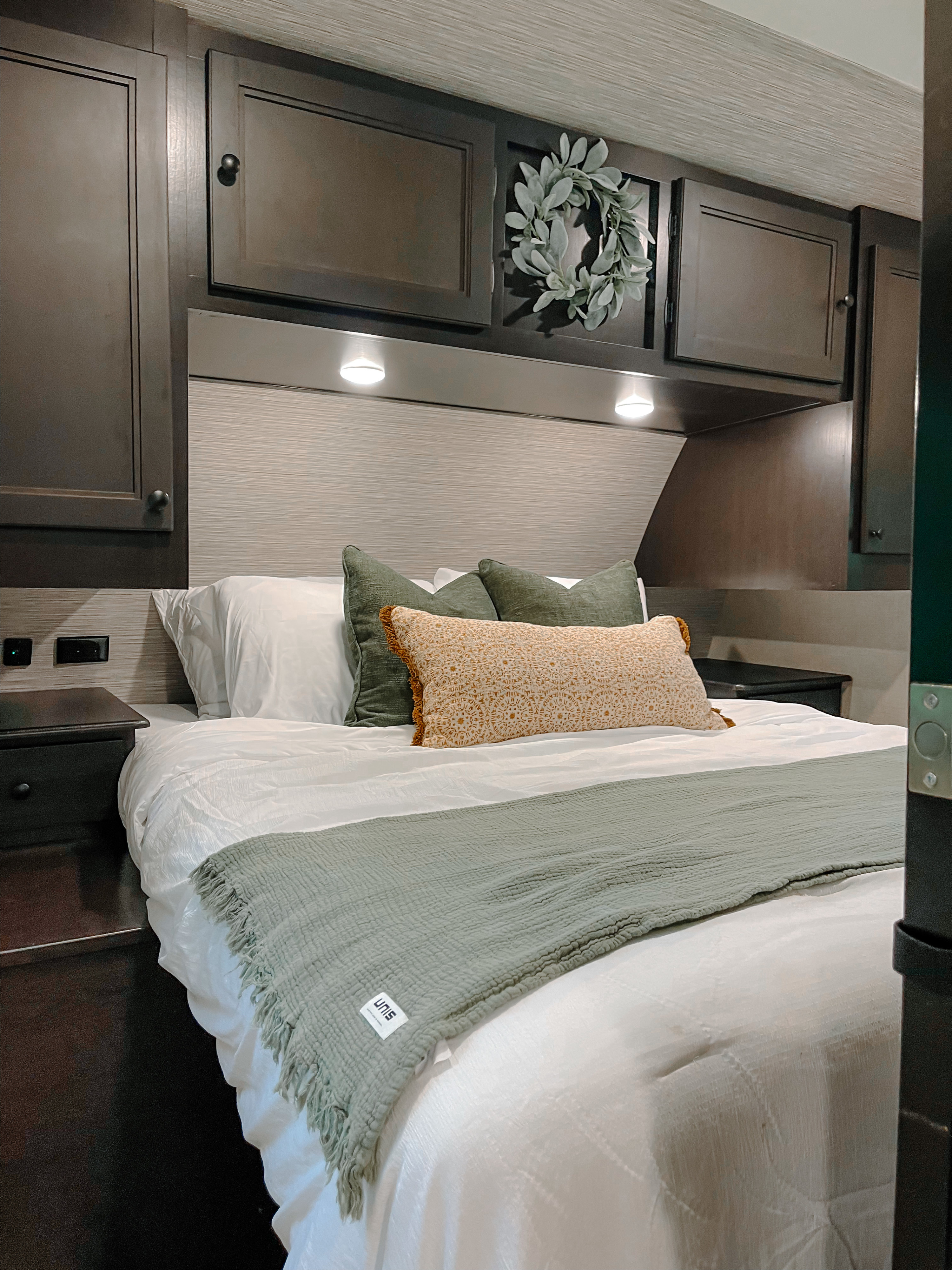 Cozy RV rental bedroom: dark wood cabinets, ambient lights, a plush bed with green and orange pillows. Ideal for your next trip.. Highland Ridge RV Range Lite 2022