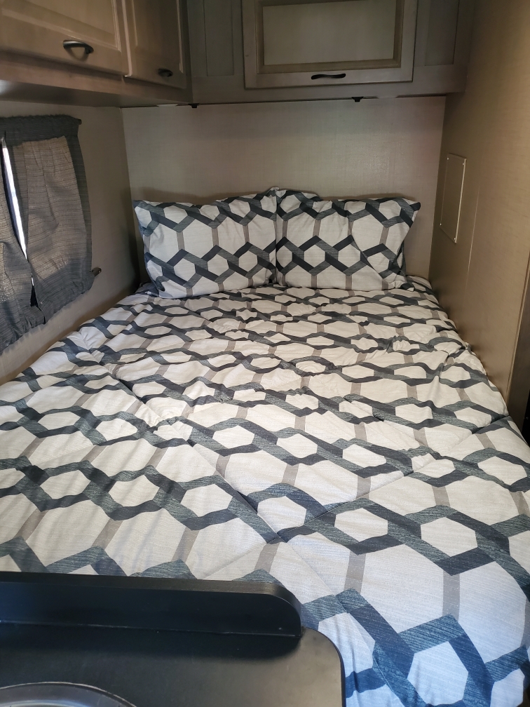 Cozy RV rental bedroom with a bed featuring gray and white geometric bedding, pillows, and overhead storage.. Thor Majestic 2018