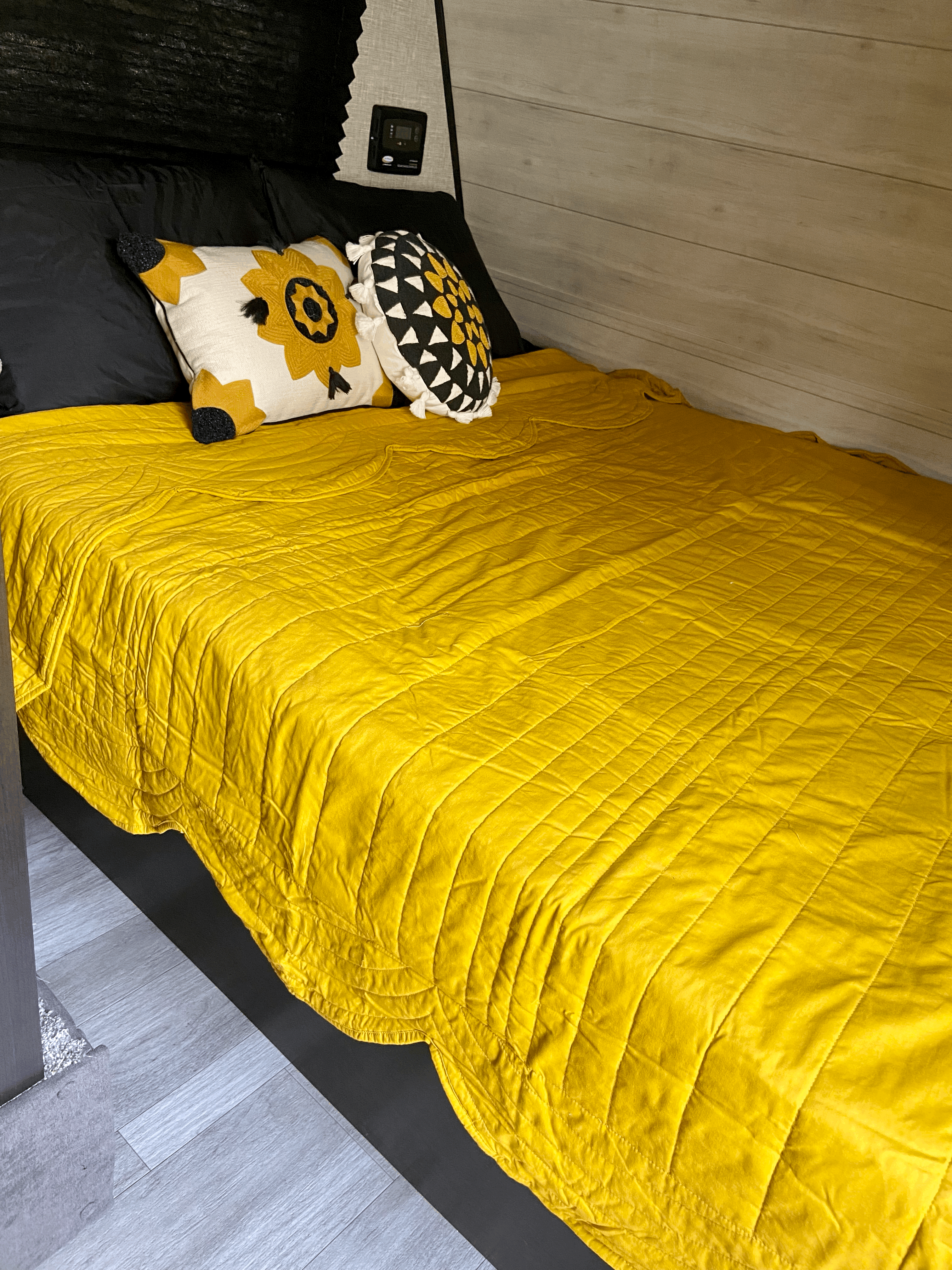 Vibrant yellow quilt on a cozy RV rental bed with black and sunflower pillows, set against wood paneling.. Jayco Jay Flight Baja 2022