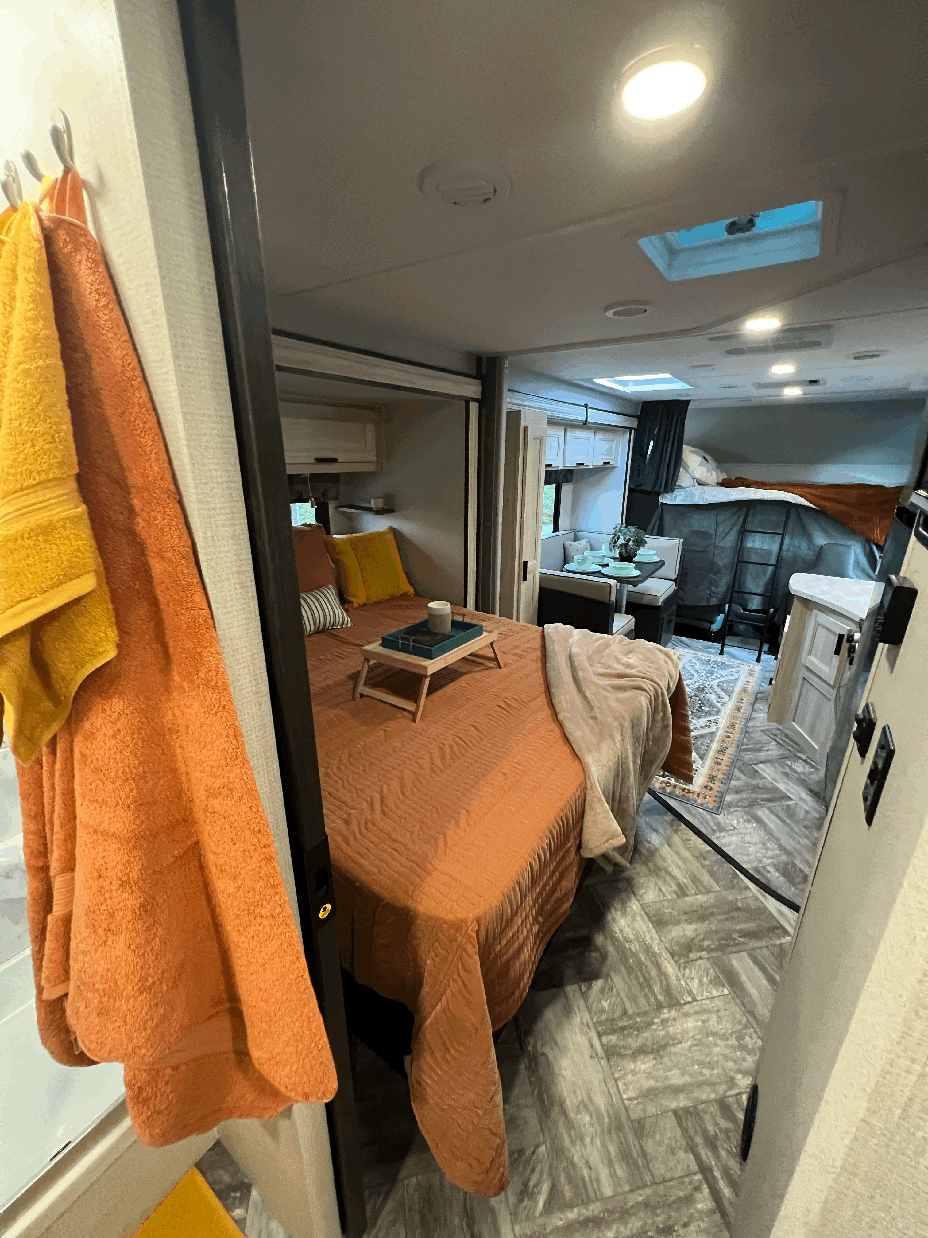 This rv rental features a cozy bedroom with orange bedding, dining area, and bunk beds. Ideal for family travel.. Forest River Sunseeker 2023