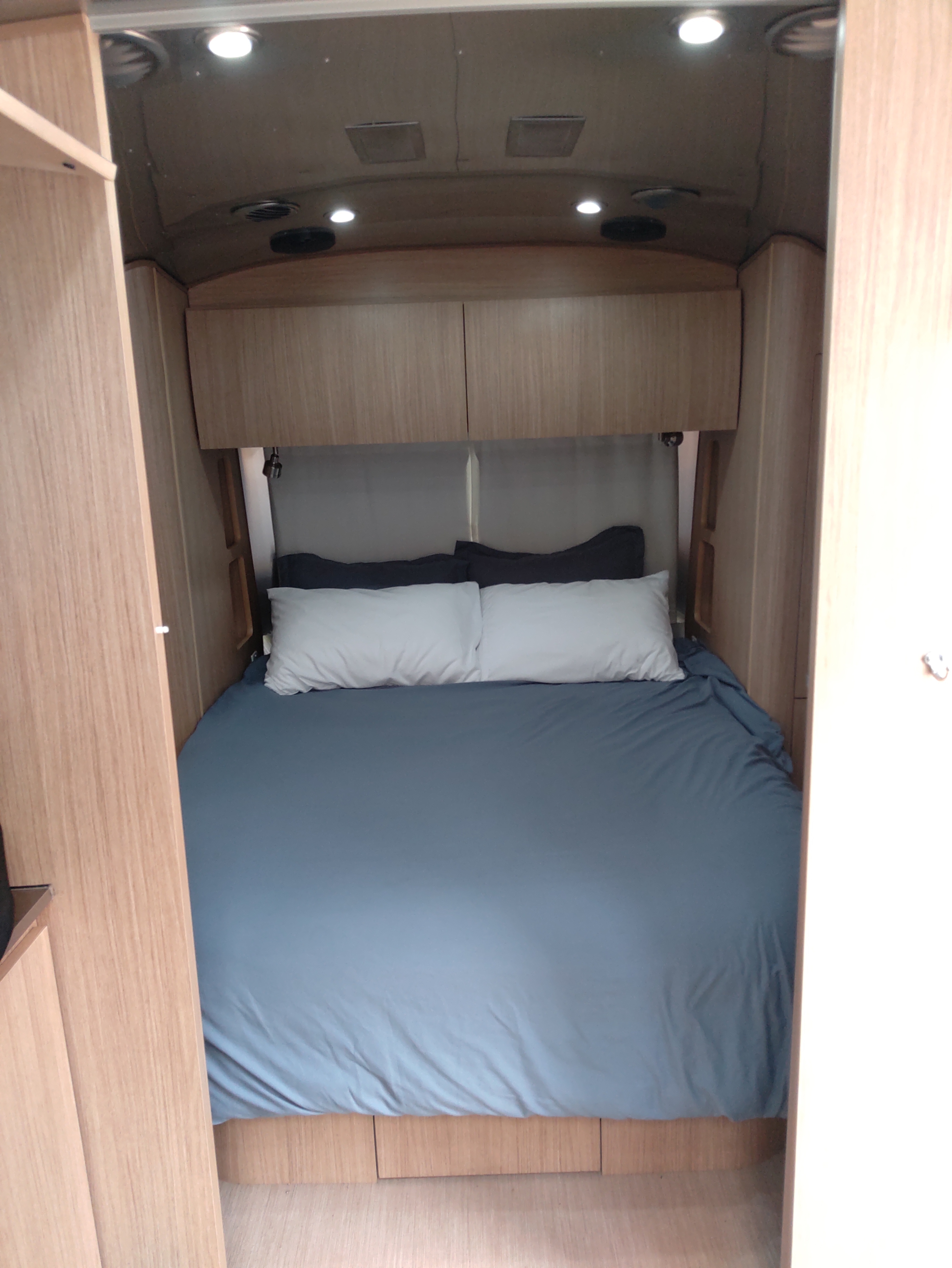 Comfortable RV rental bedroom featuring a neatly made bed with blue bedding and wooden overhead cabinets.. Airstream Flying Cloud 2018