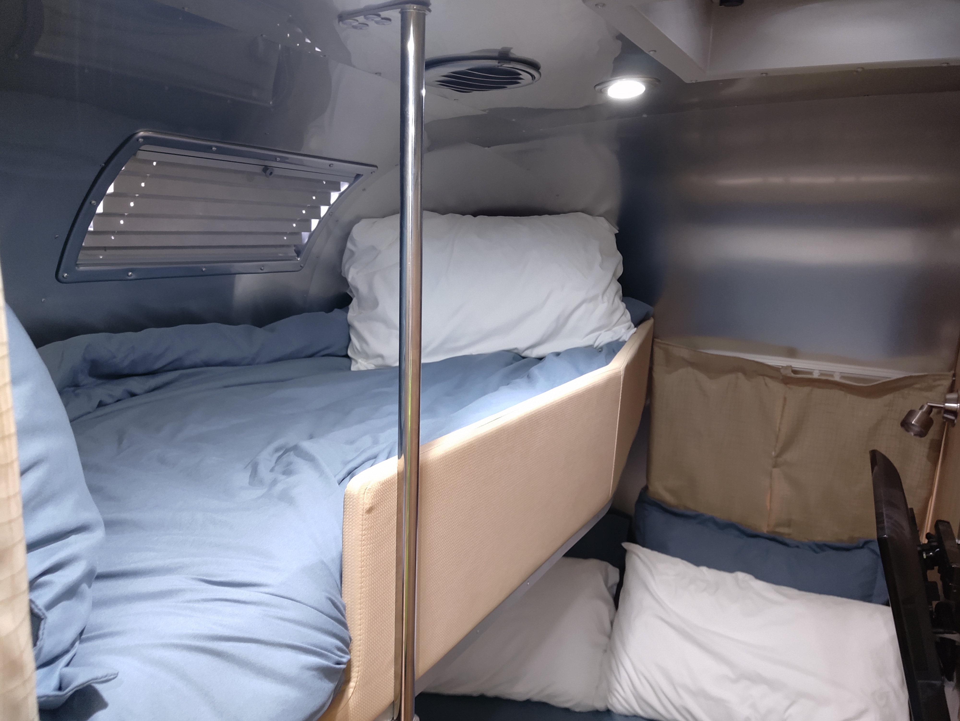 Cozy bunk beds in an RV rental, featuring blue bedding, a window, and a reading light, perfect for campers.. Airstream Flying Cloud 2018