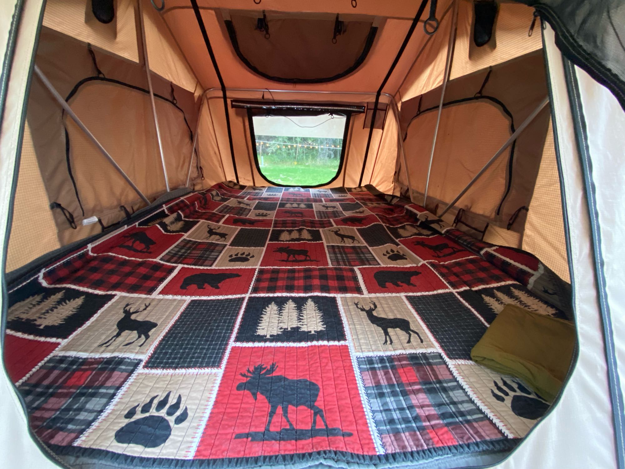 Cozy RV rental rooftop tent interior: nature-themed quilt, open window view. Ready for adventure!. Jeep Rubicon 2014