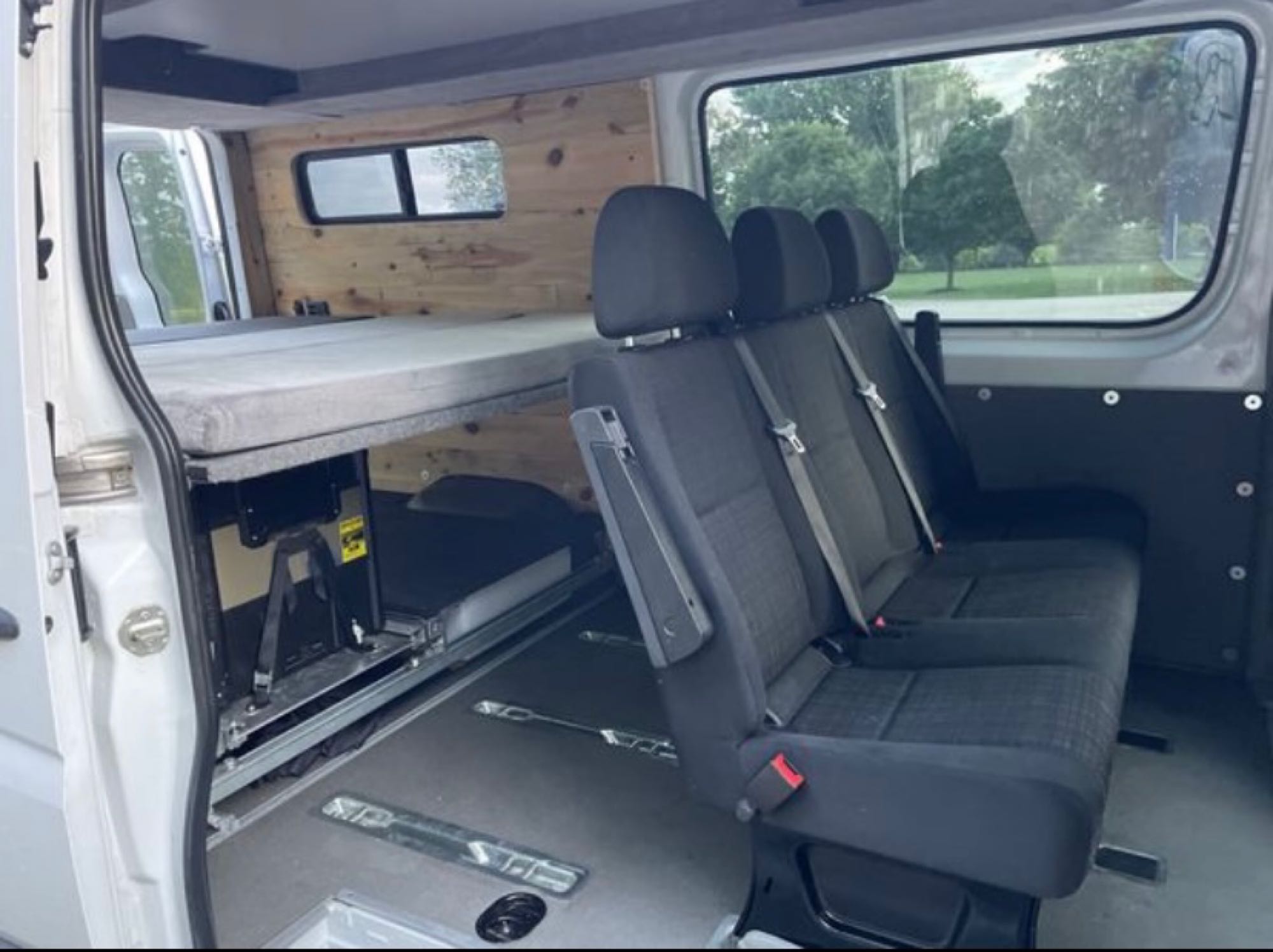 Versatile camper van interior for RV rental, showcasing a raised bed, flexible seating for three, and smart storage solutions.. Freightliner Sprinter 2015
