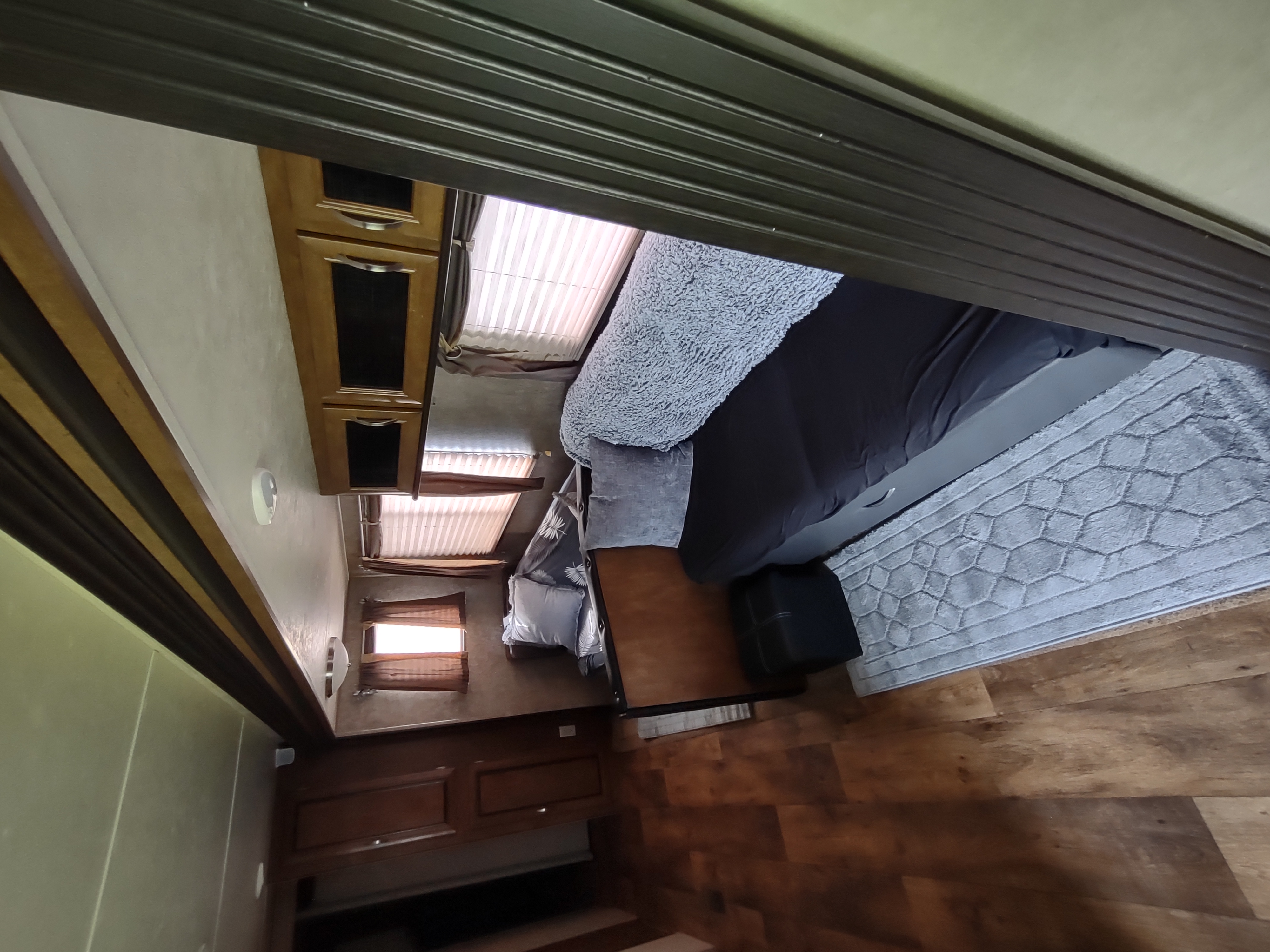 Cozy RV rental bedroom featuring a large bed, patterned rug, wood floor, and overhead storage.. Forest River Salem 2017