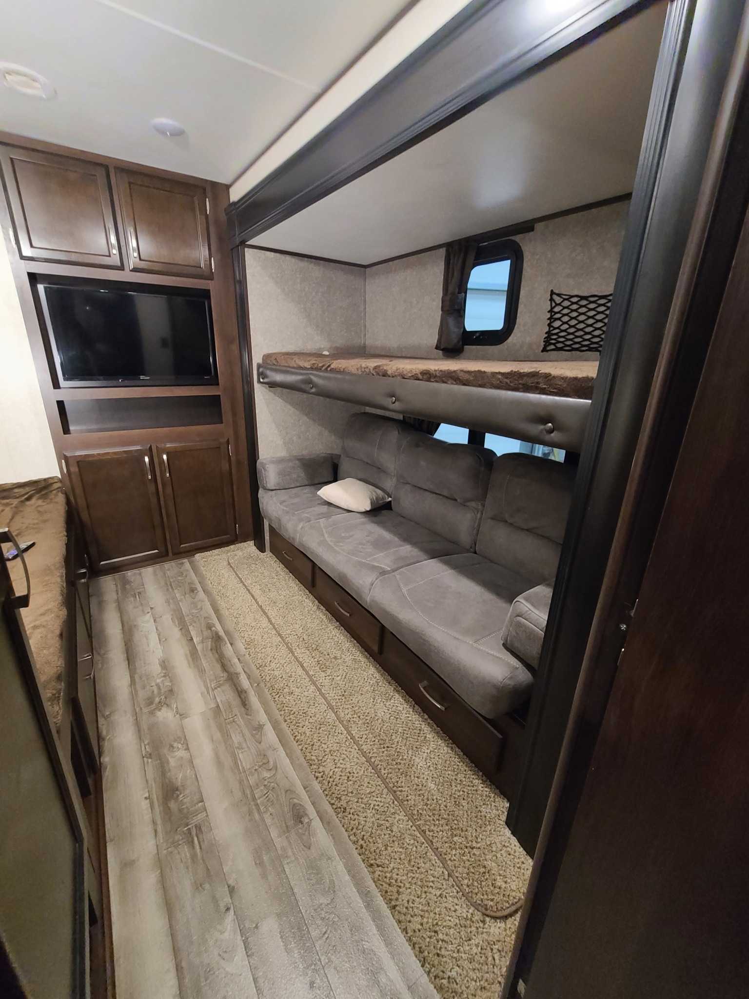 View inside an RV rental bunkhouse: compact living area with sofa, upper bed, and TV, ideal for family trips.. Jayco Jay Flight 2020
