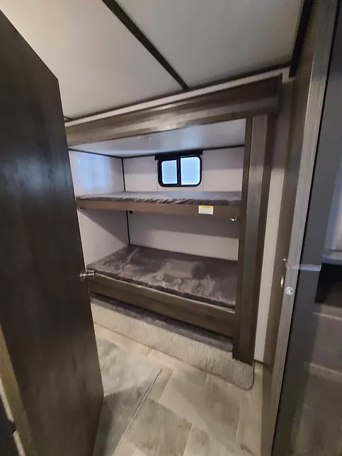 Inside an RV rental: A well-lit bunk bed area with two stacked beds and a small window, offering cozy sleeping space for travel.. Coleman Lantern 32BHDS 2021