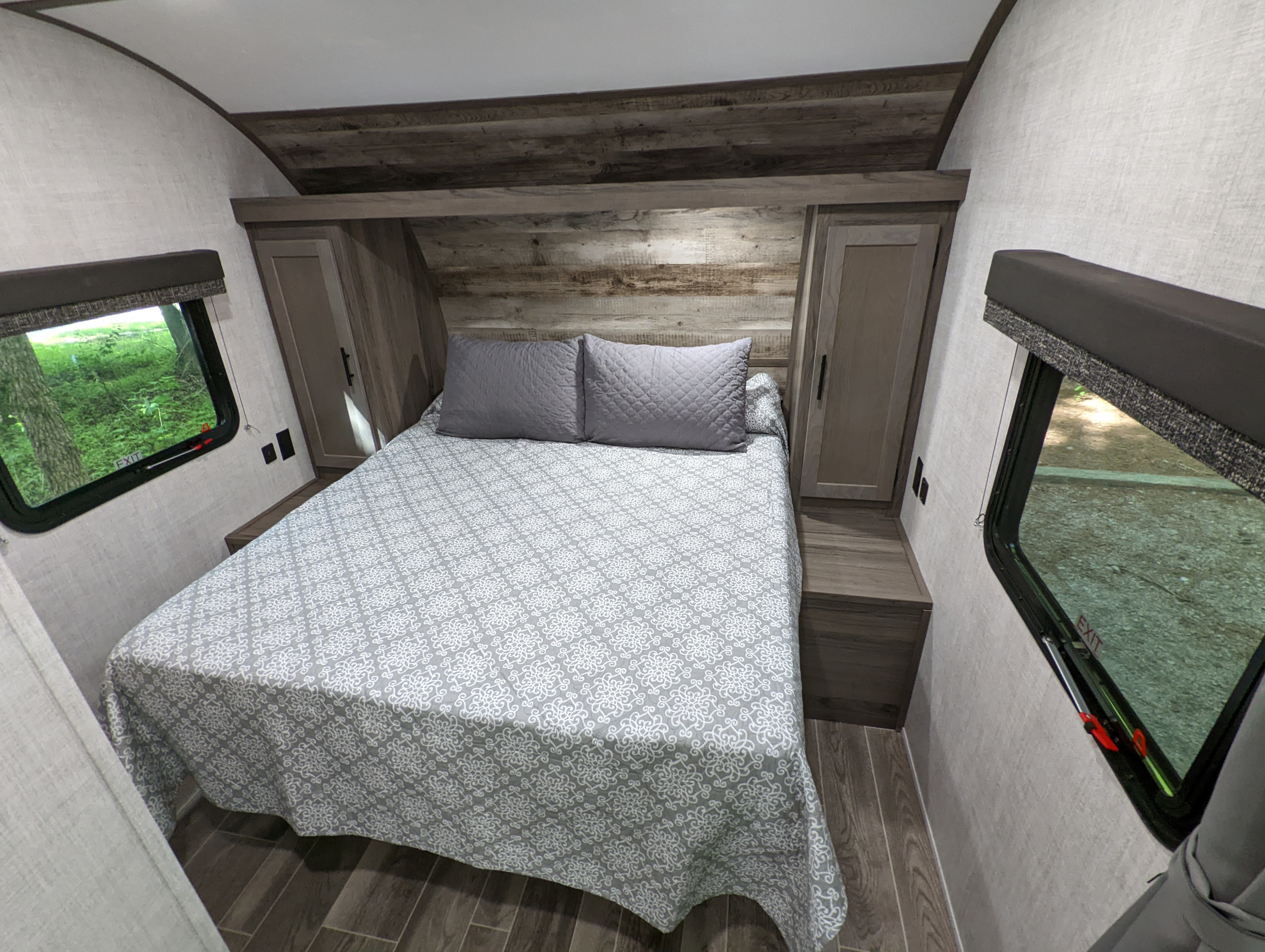 This RV rental bedroom offers a comfortable bed with patterned cover, wood paneling, and natural light from side windows.. Gulf Stream Kingsport 2022