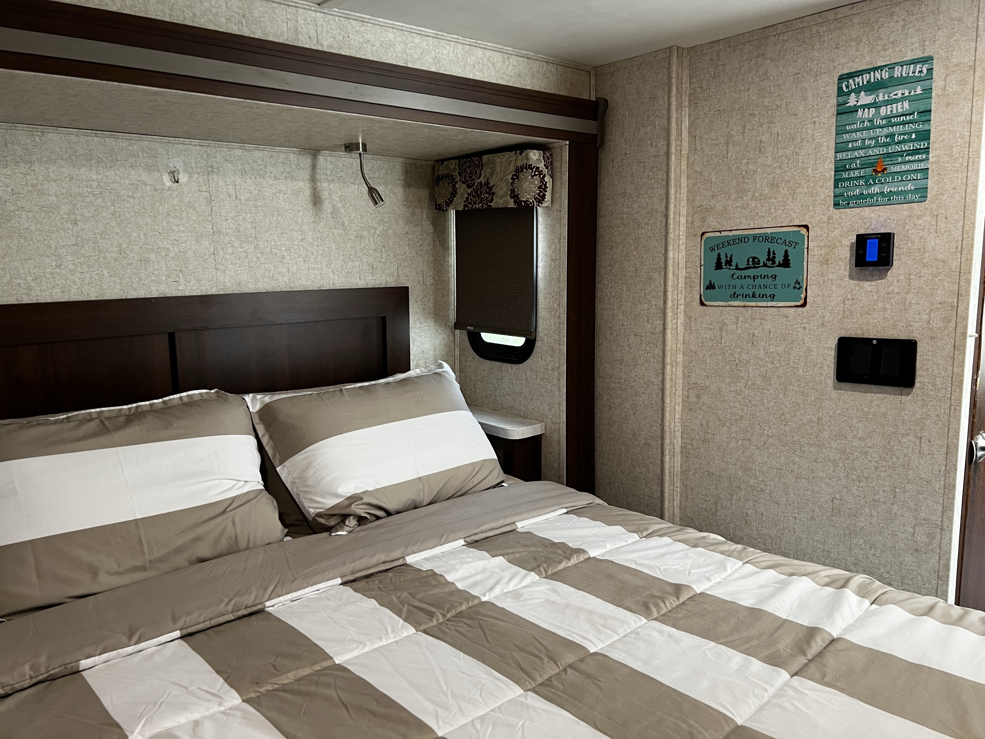 Cozy RV rental bedroom with striped bedding, headboard, read lights, and fun camping signs. RV controls visible.. Forester Forester Motorhome 2019