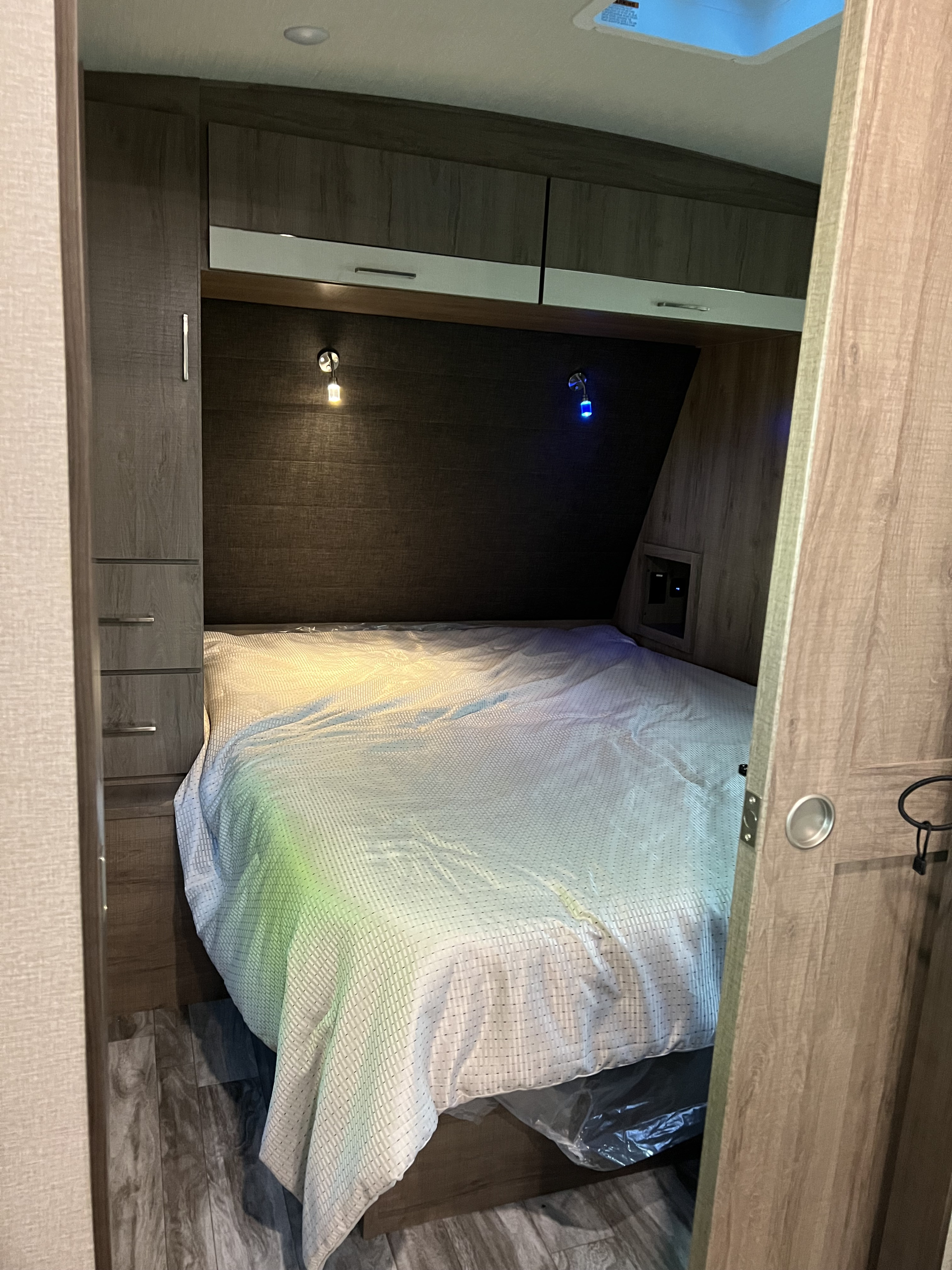 Cozy RV rental bedroom: bed with textured white blanket, overhead cabinets, and bedside lights (one yellow, one blue).. Grand Design Imagine 2800 BH 2022