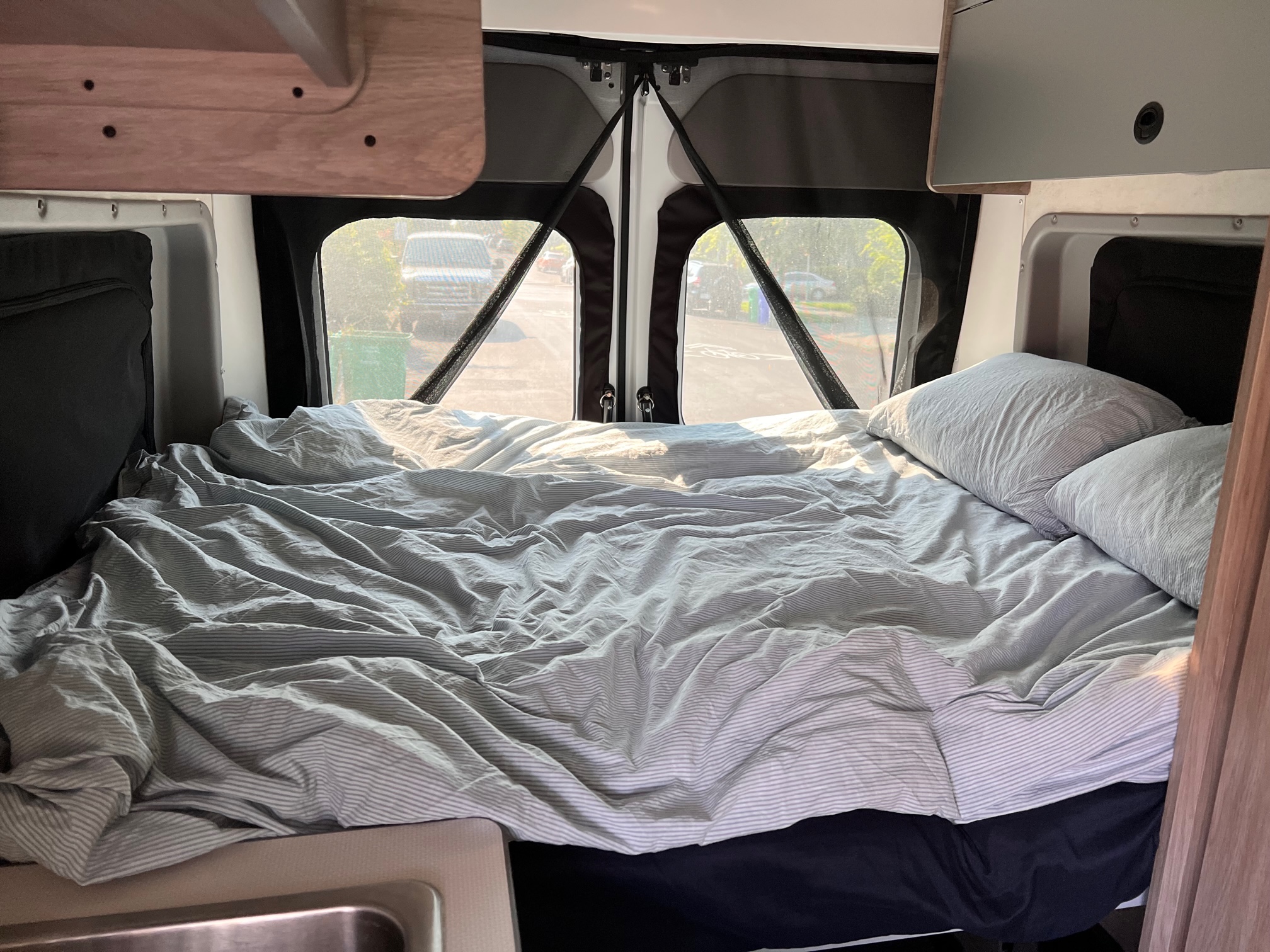 RV rental interior featuring a comfy bed with striped linens at the rear, offering views through screened windows.. Winnebago Solis 2022