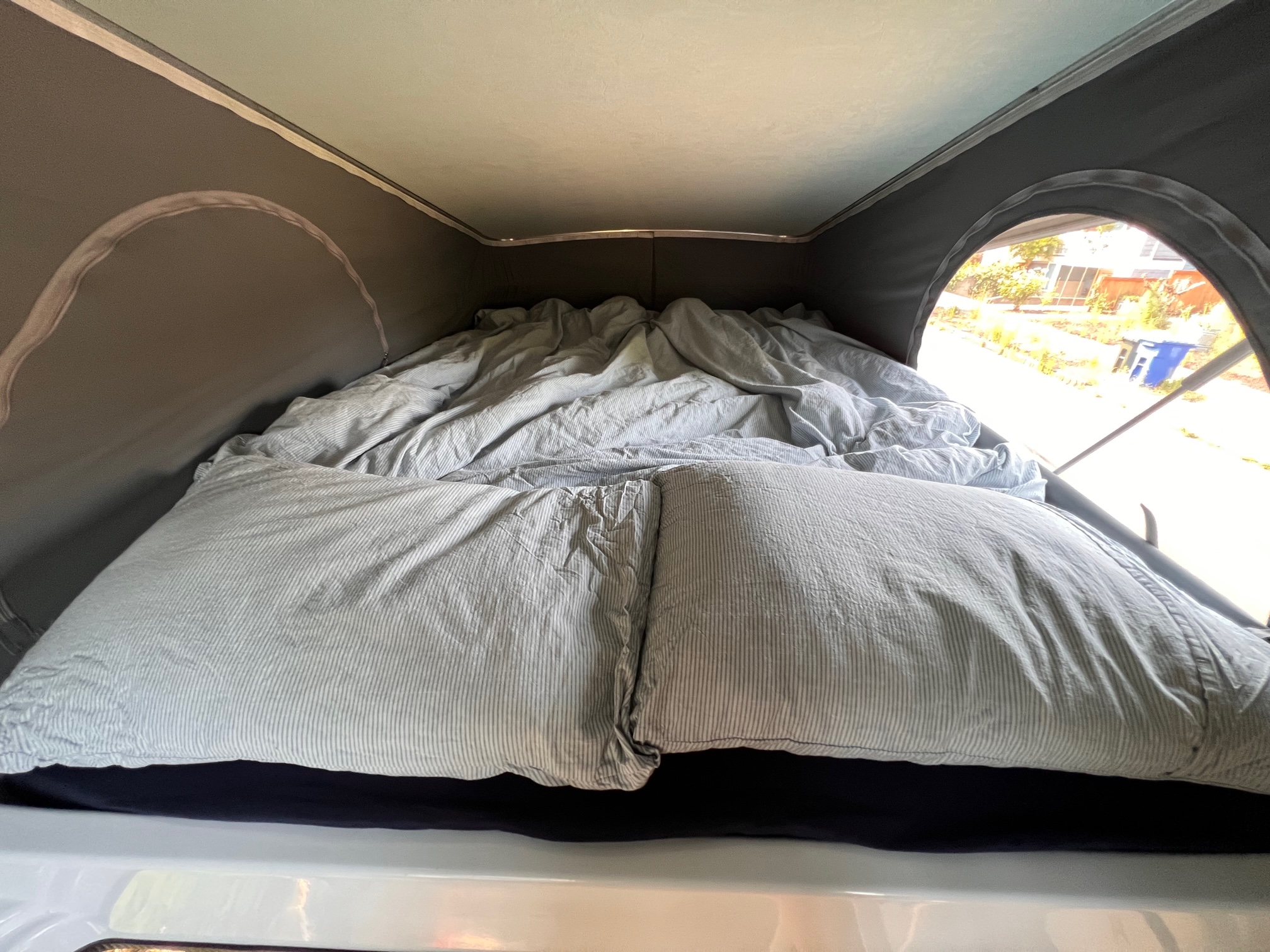 Cozy interior of an RV rental pop-top, featuring a comfortable bed with light-striped bedding, ideal for camping adventures.. Winnebago Solis 2022