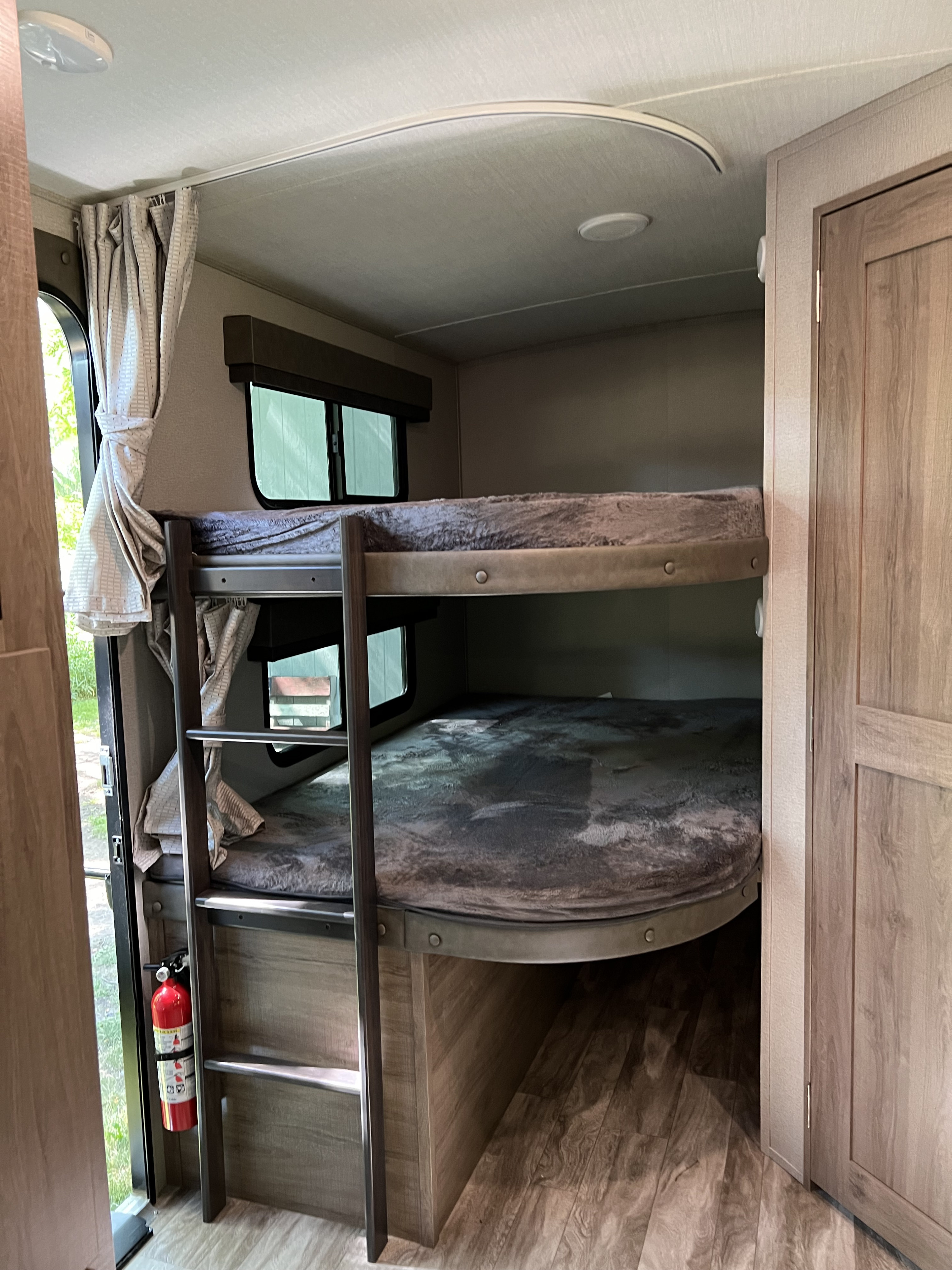 Inside an RV rental: two bunk beds with ladder, windows, and a fire extinguisher for safety.. Grand Design Imagine 2800 BH 2022