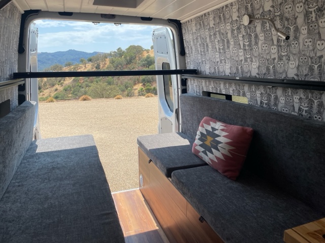 RV rental with comfy grey benches, owl wallpaper, and a metal bar. Enjoy mountain views from this camper van interior.. Mercedes-Benz Sprinter 2021