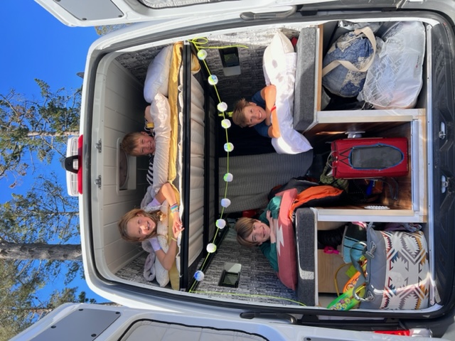 Four smiling kids peek from cozy bunks and storage cubbies inside a fun RV rental camper van, ready for family adventures.. Mercedes-Benz Sprinter 2021