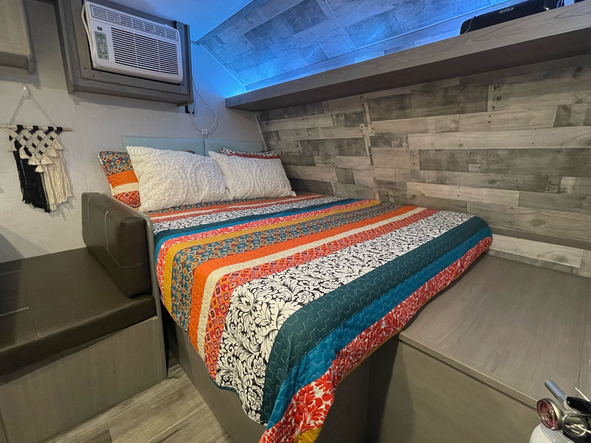 Explore this modern RV rental interior featuring a comfy bed, wood-paneled walls with blue light, and a compact AC unit.. Dutchmen Coleman Lantern LT 2022
