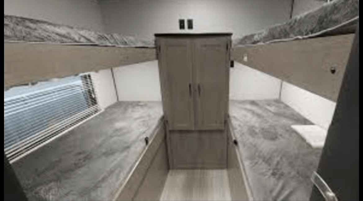 This RV rental shows a cozy bunkhouse with four beds, a central wardrobe, and a window, perfect for families.. Keystone RV Hideout 2020
