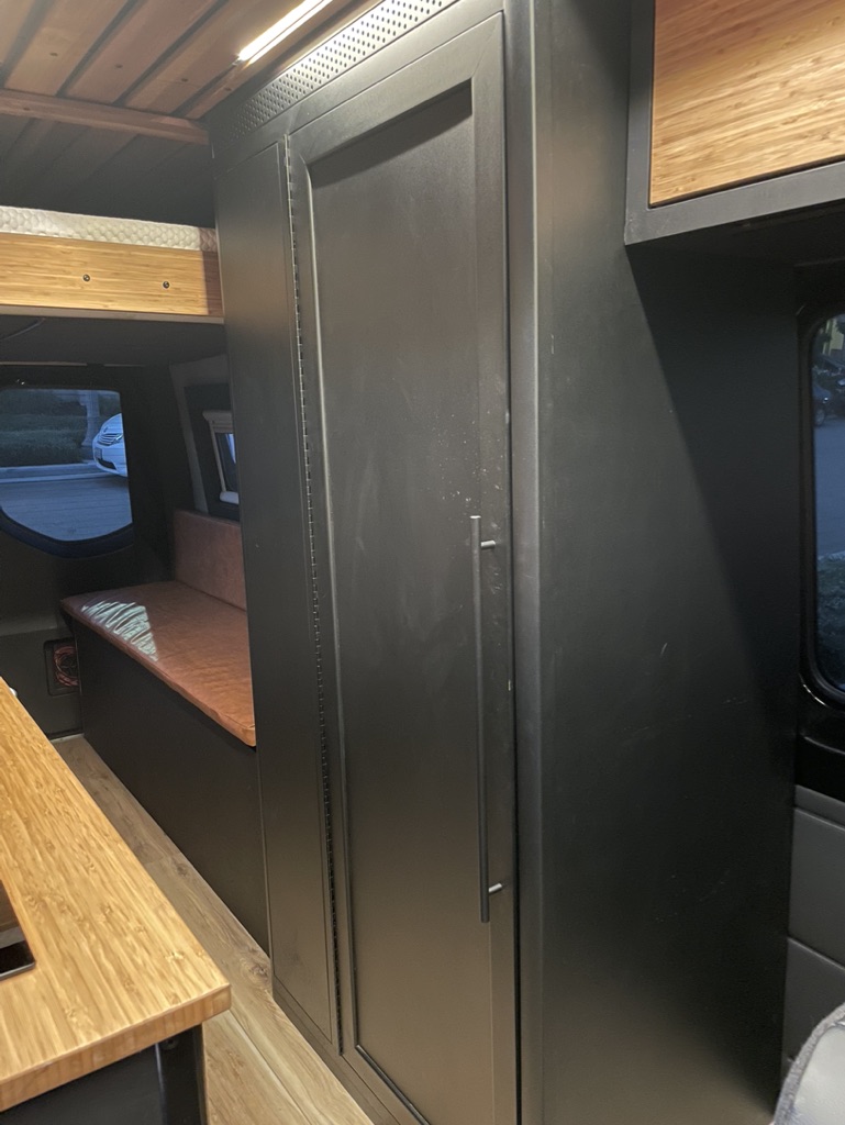 Inside a modern RV rental: a black wardrobe, wooden counters, bunk bed, and bench seating offer compact living solutions.. Mercedes-Benz Sprinter 2019