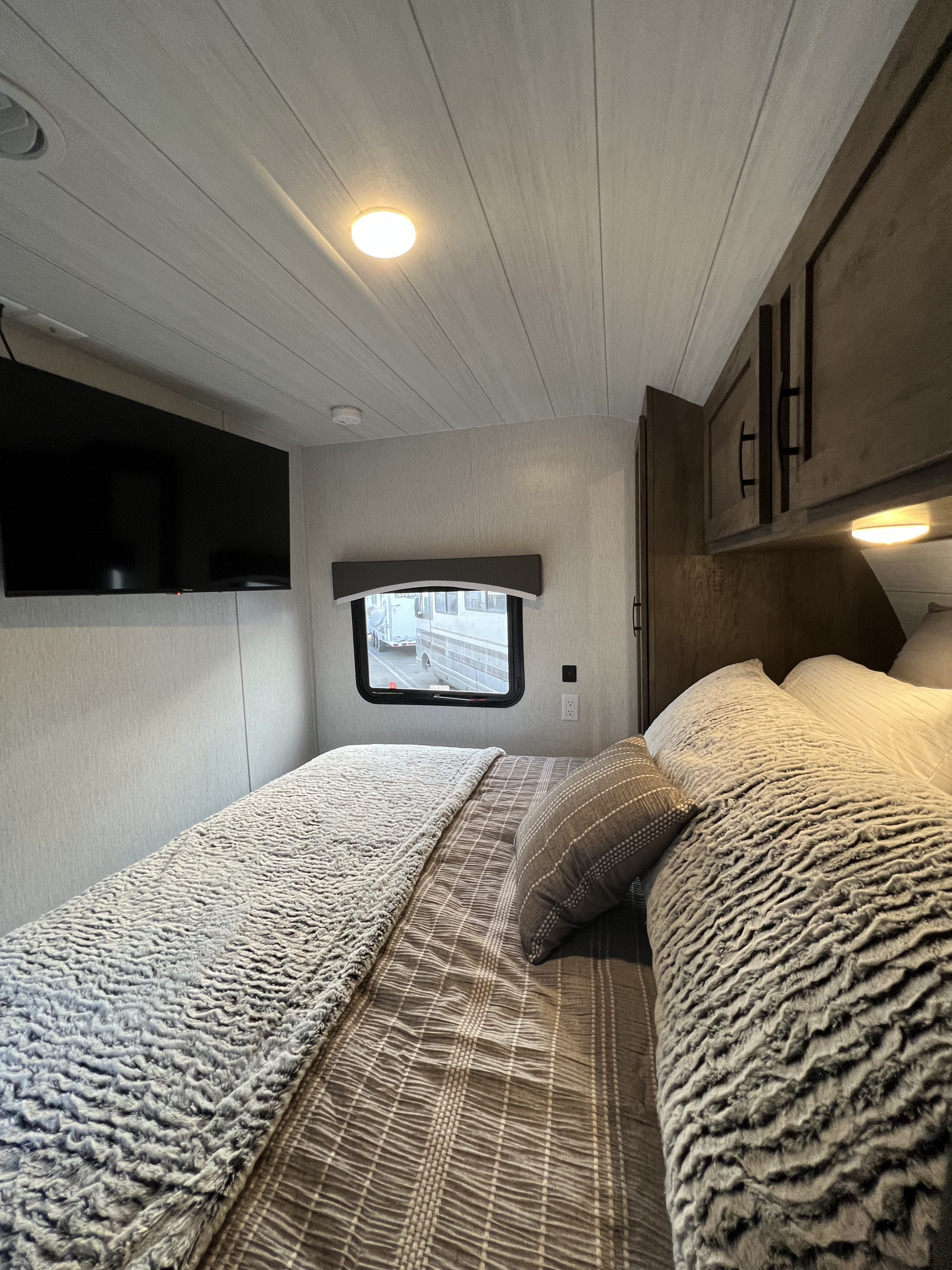 RV rental: The bedroom features a mounted TV, overhead cabinets, window view, and cozy patterned bedding.. Forest River EVO T2850 2022