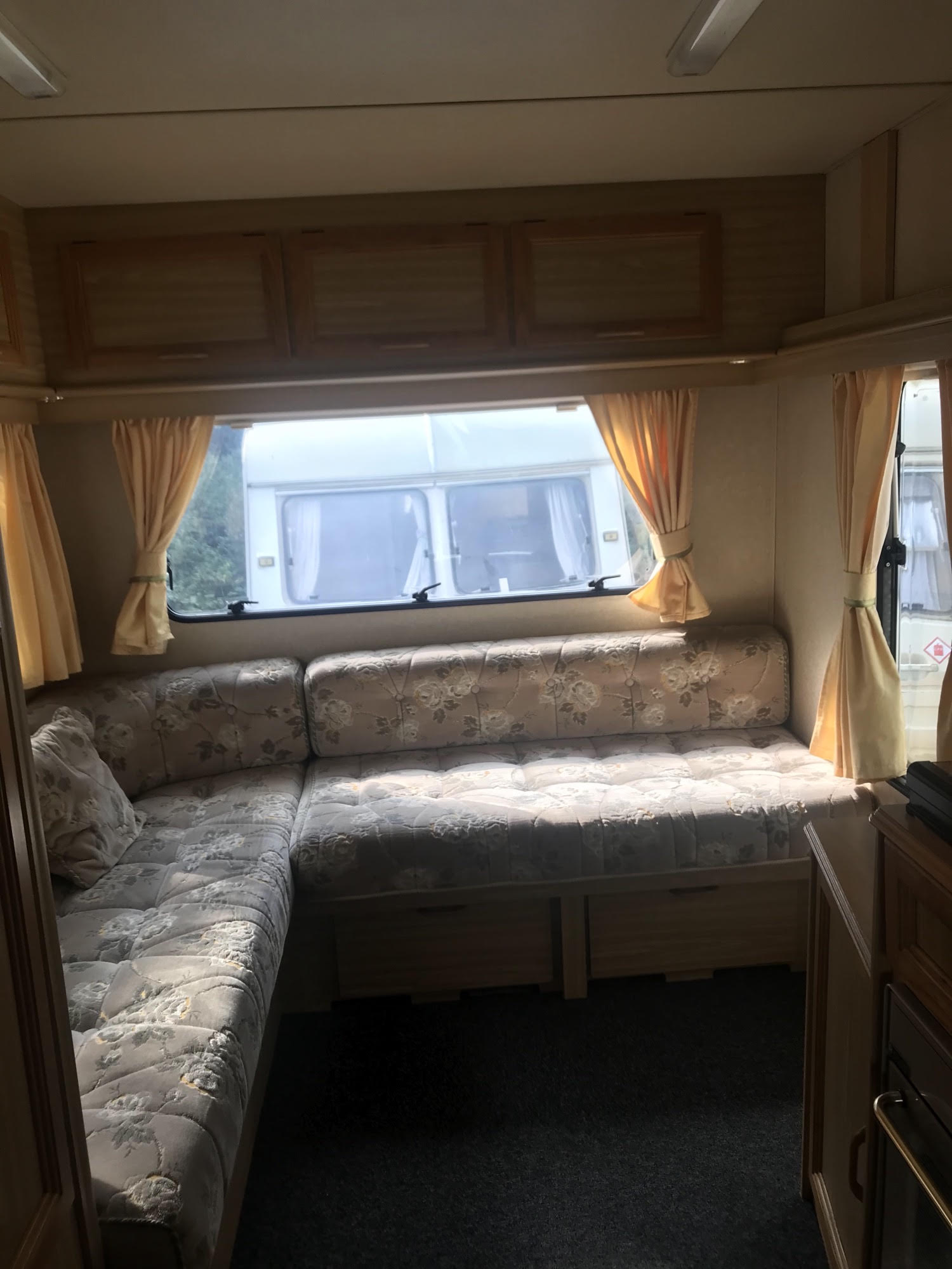 Cozy RV rental interior with floral-patterned U-shaped seating, wooden overhead cabinets, and sunlit windows.. Peugeot Boxer 270 MWB 1998
