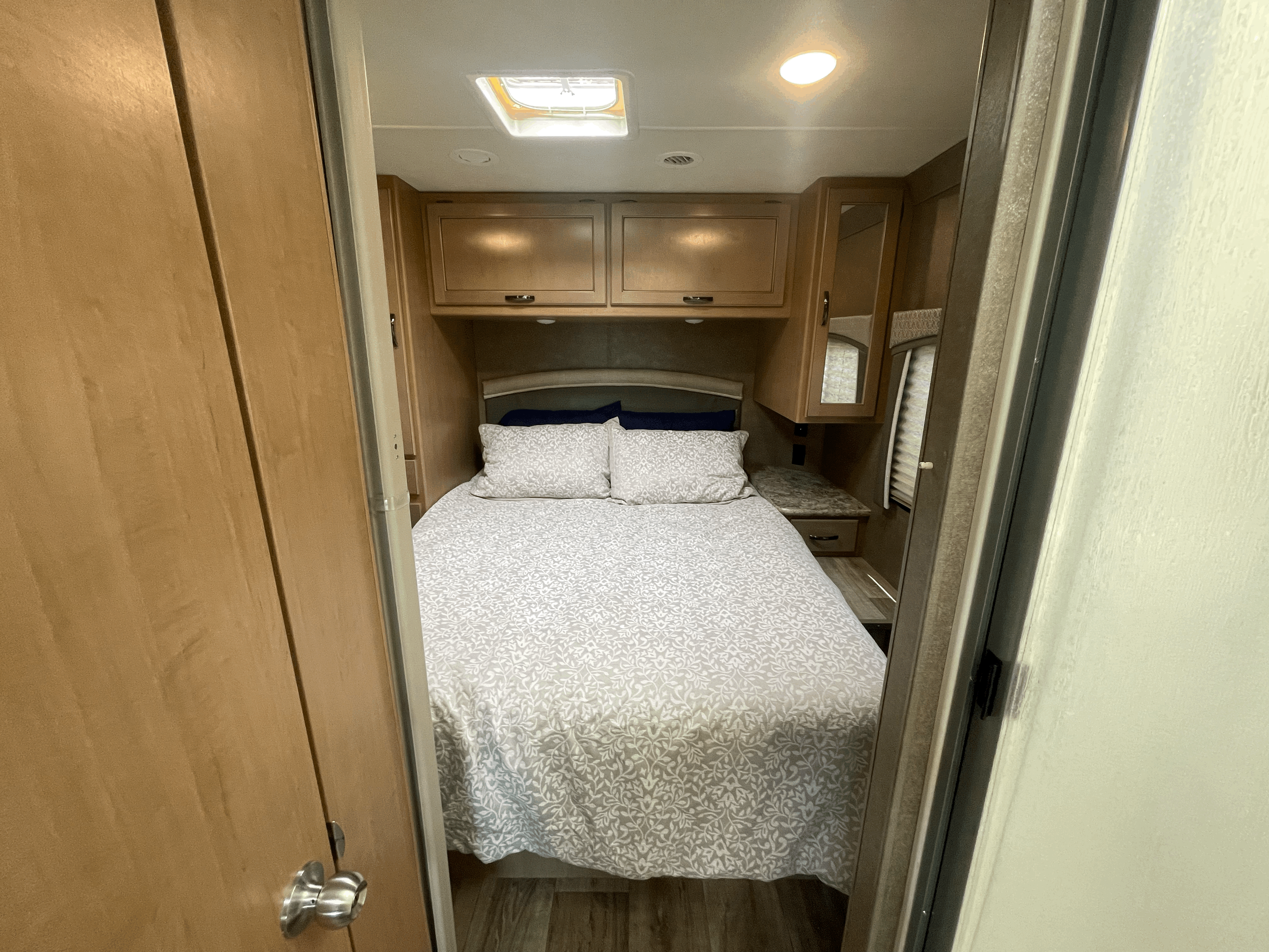 Comfortable RV rental bedroom with patterned bedding, wood cabinets, and skylight.. Thor Four Winds 2021