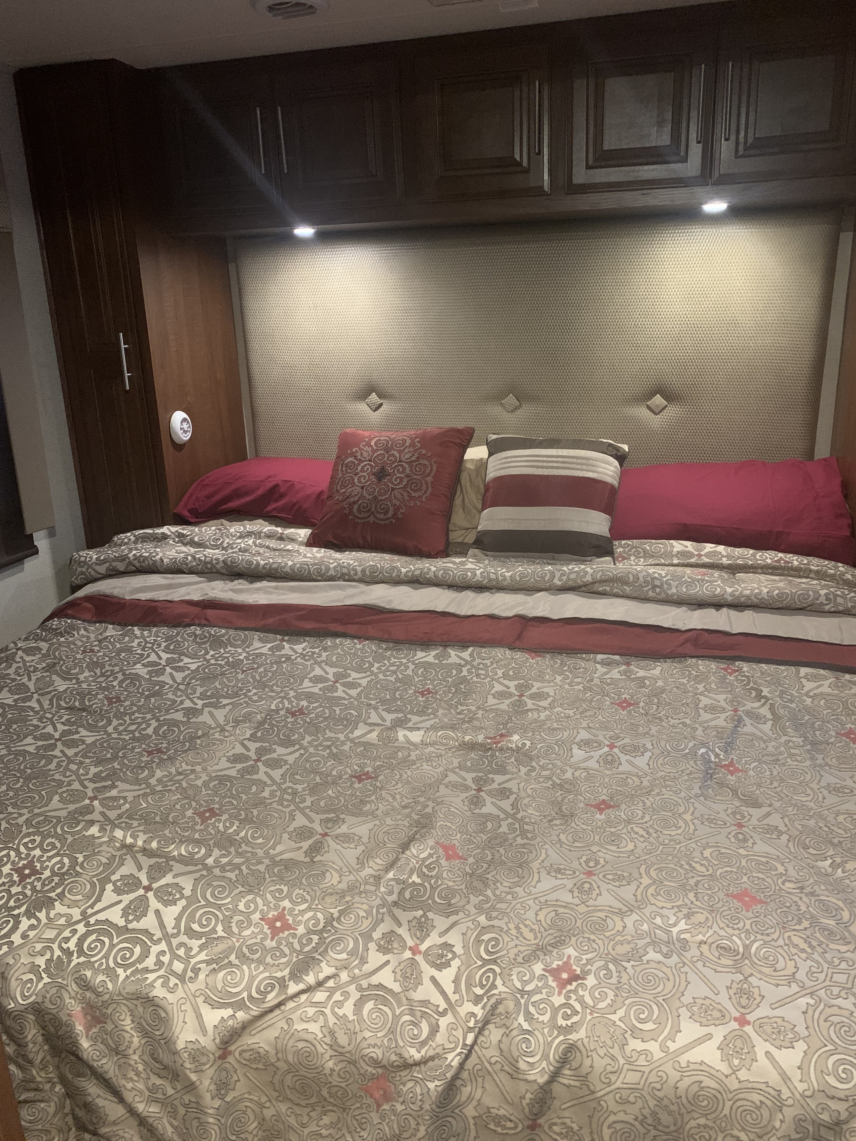 RV rental bedroom showcasing a comfortable bed with patterned bedding, an upholstered headboard, and dark wood overhead cabinets.. Georgetown Georgetown Motorhome 2017